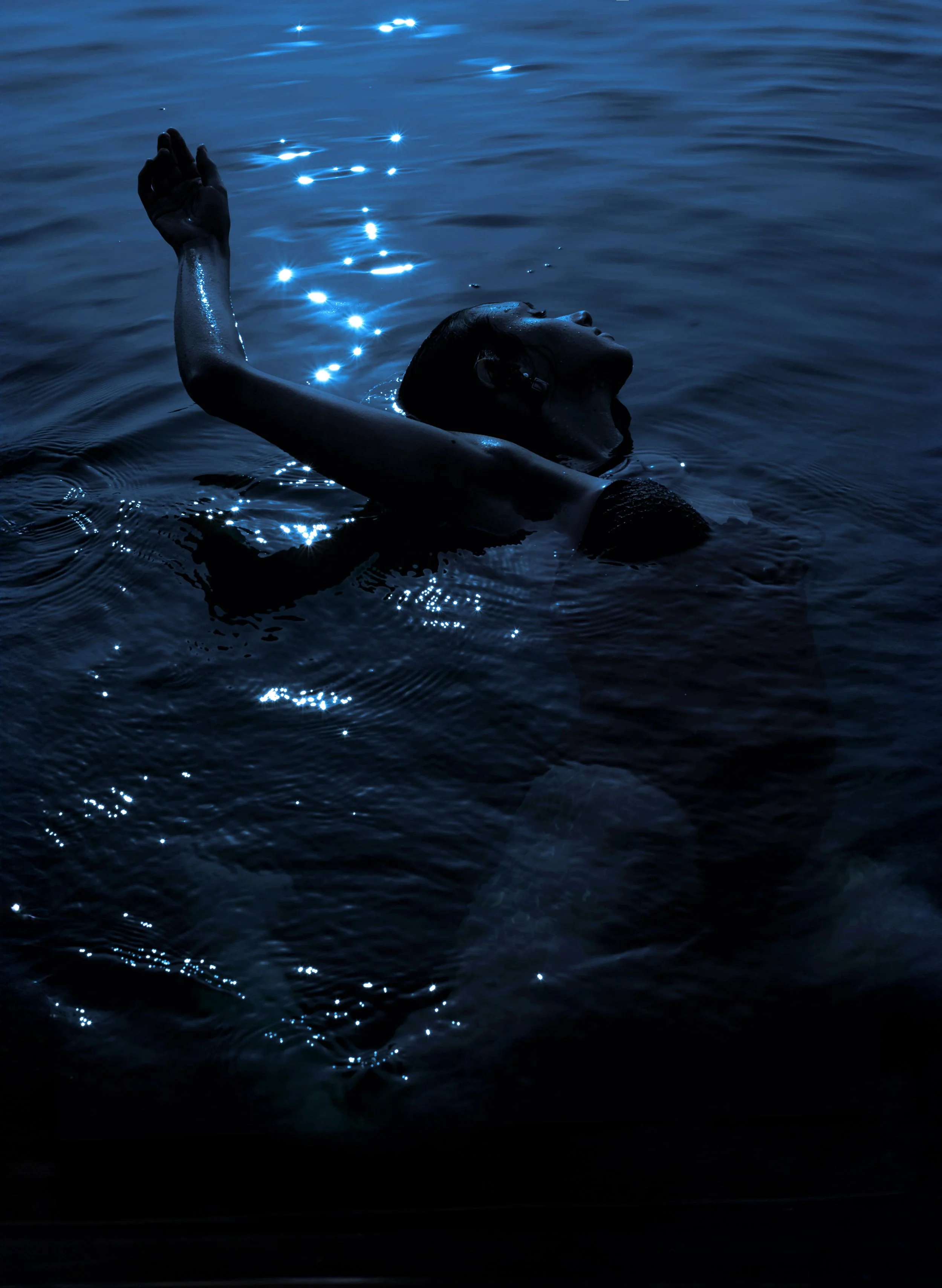 Persona che nuota di notte in acqua illuminata dalla luna.