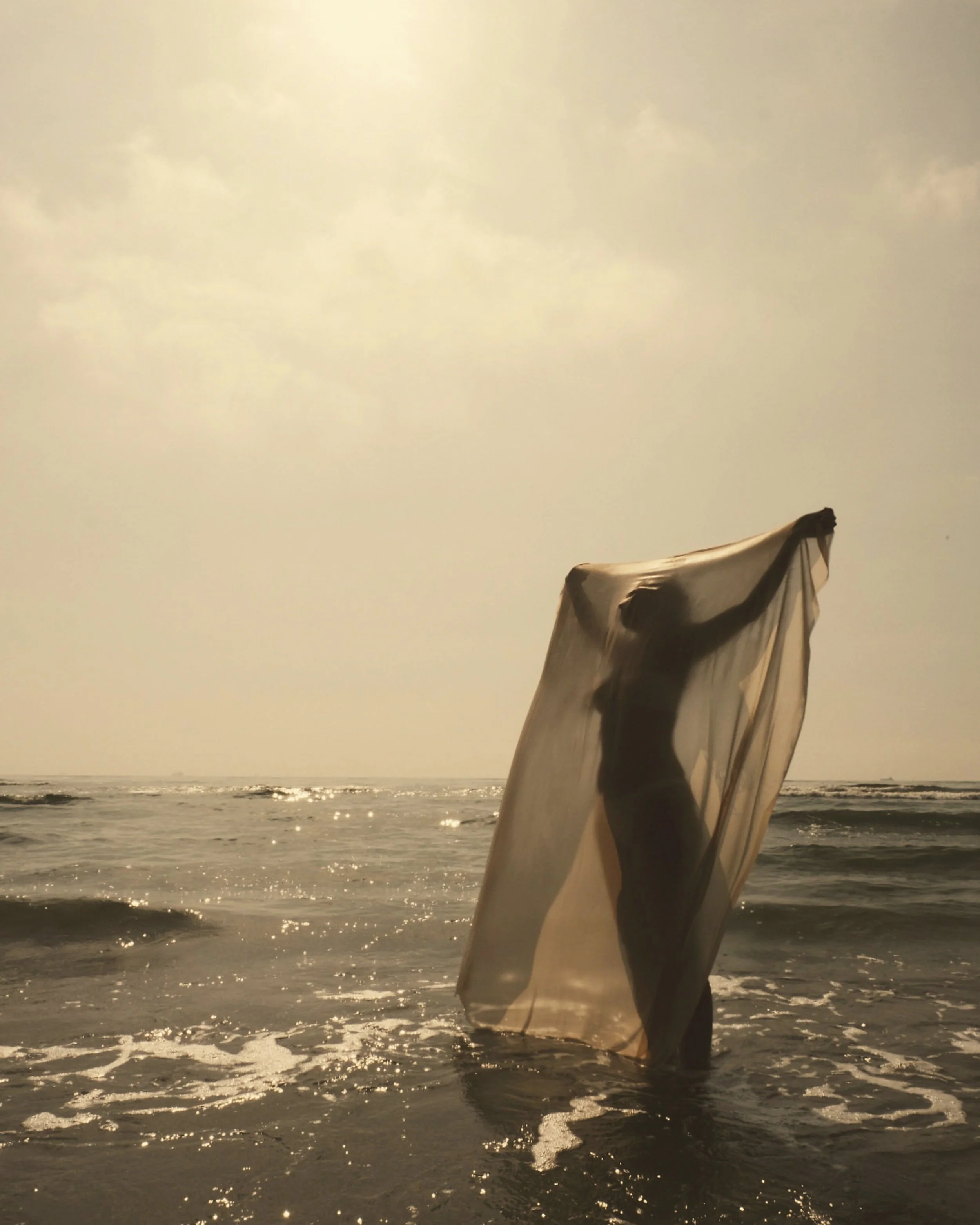 Una donna con il corpo nascosto da un telo trasparente sulla spiaggia al tramonto.