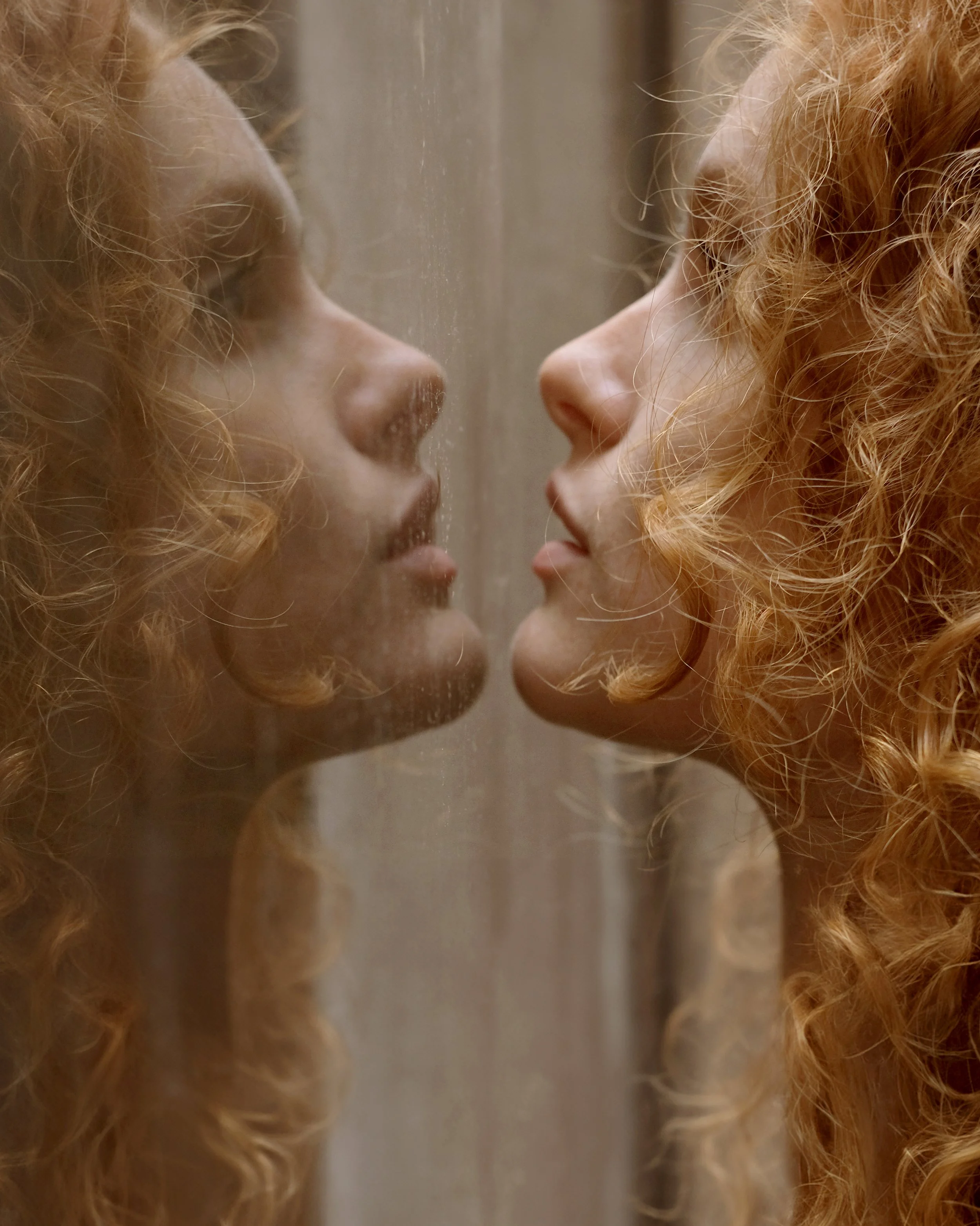 Donna con capelli ricci rossi riflessa in una superficie di vetro.