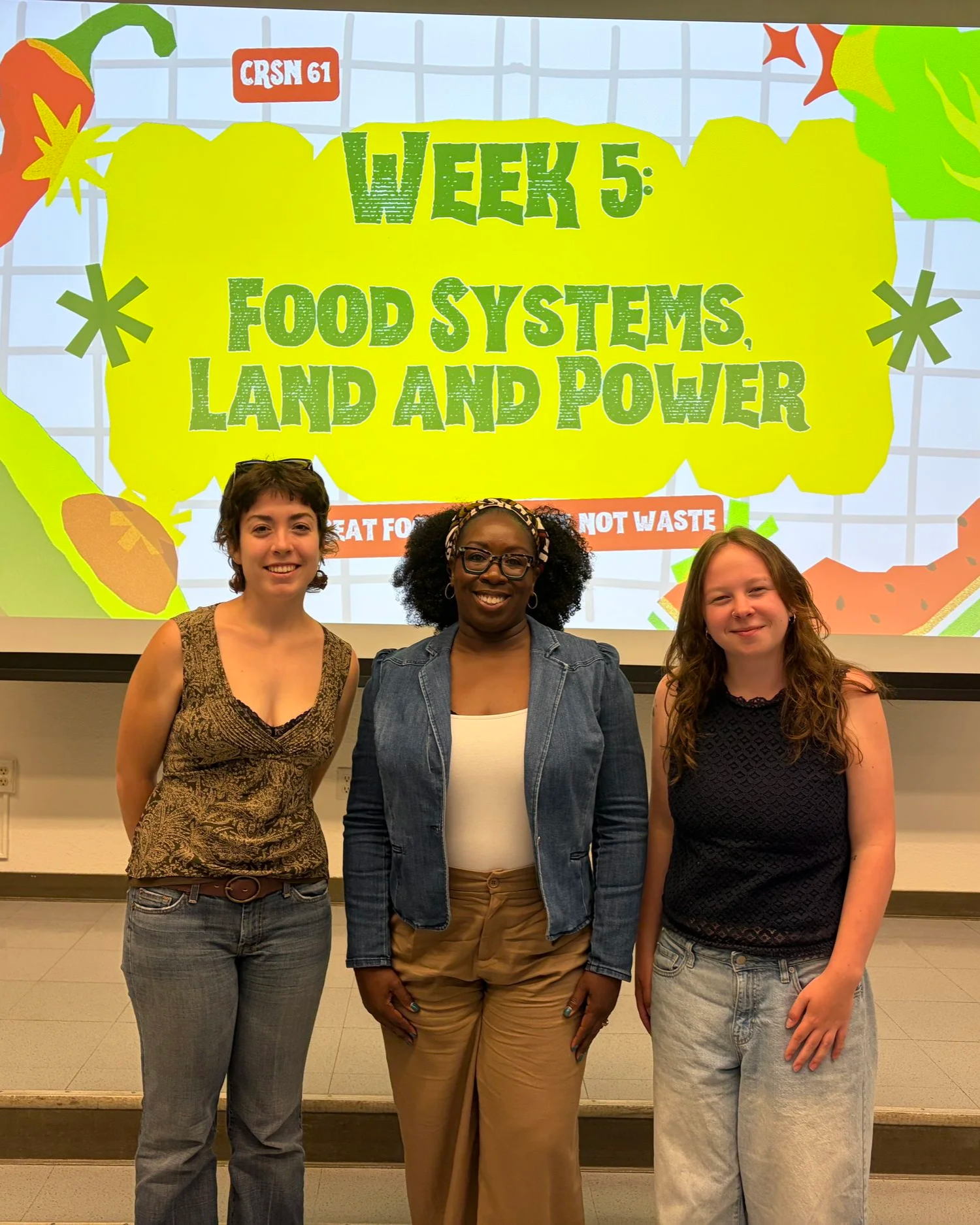 Three women standing in front of a colorful sign that reads 'Week 5: Food Systems, Land and Power' at an event or conference.