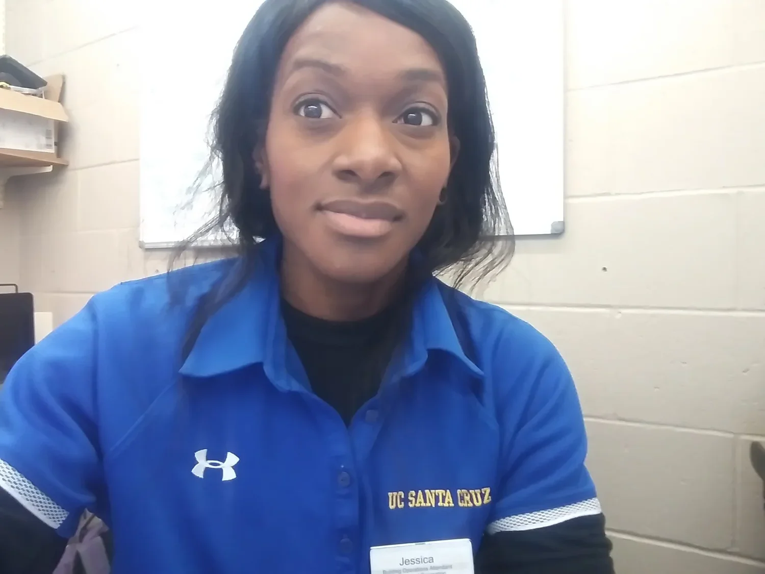 A woman with dark hair wearing a blue UC Santa Cruz shirt, sitting in a classroom or office environment.