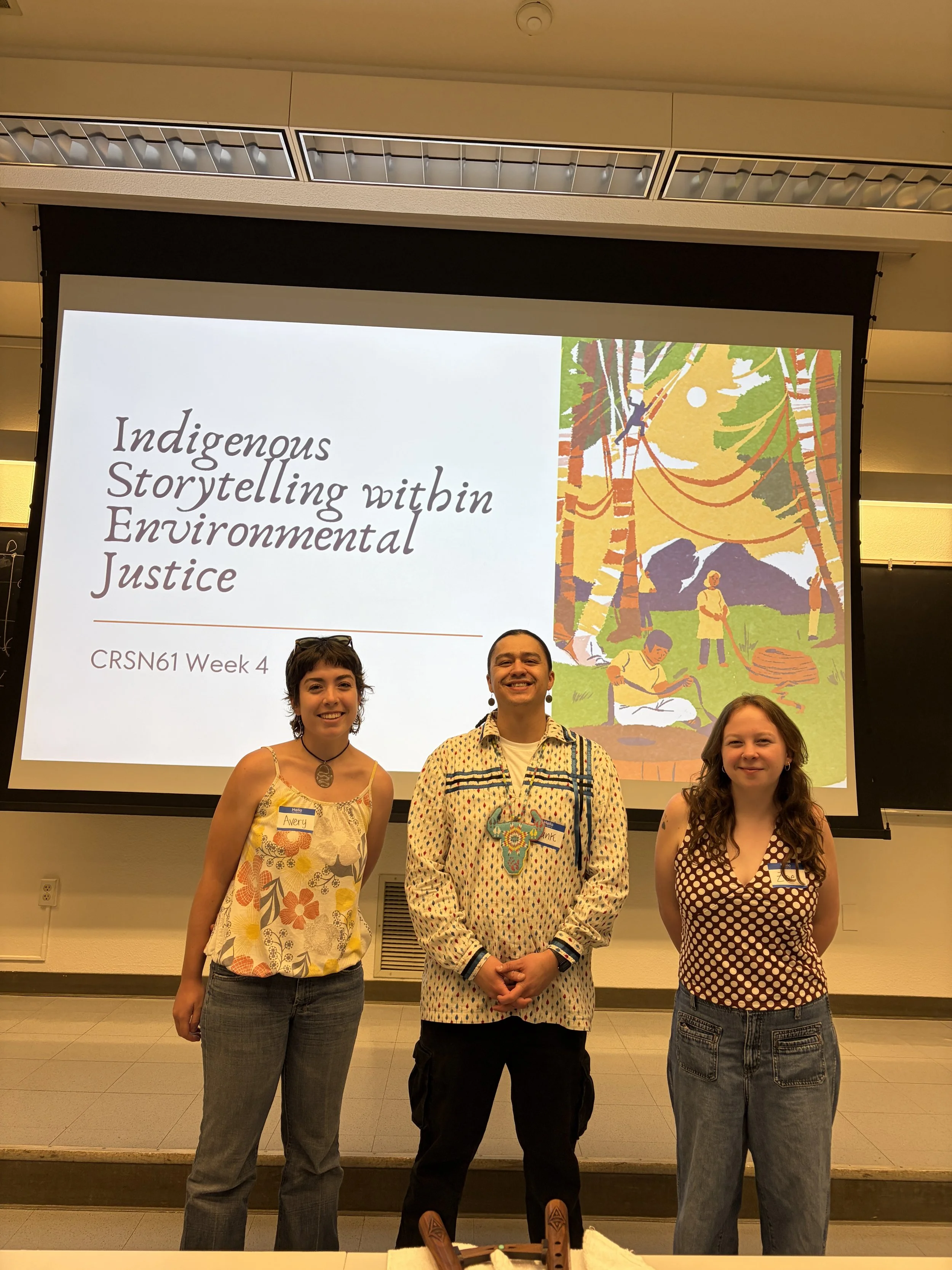 Three people standing in front of a presentation screen with the title 'Indigenous Storytelling within Environmental Justice' at a conference or event.