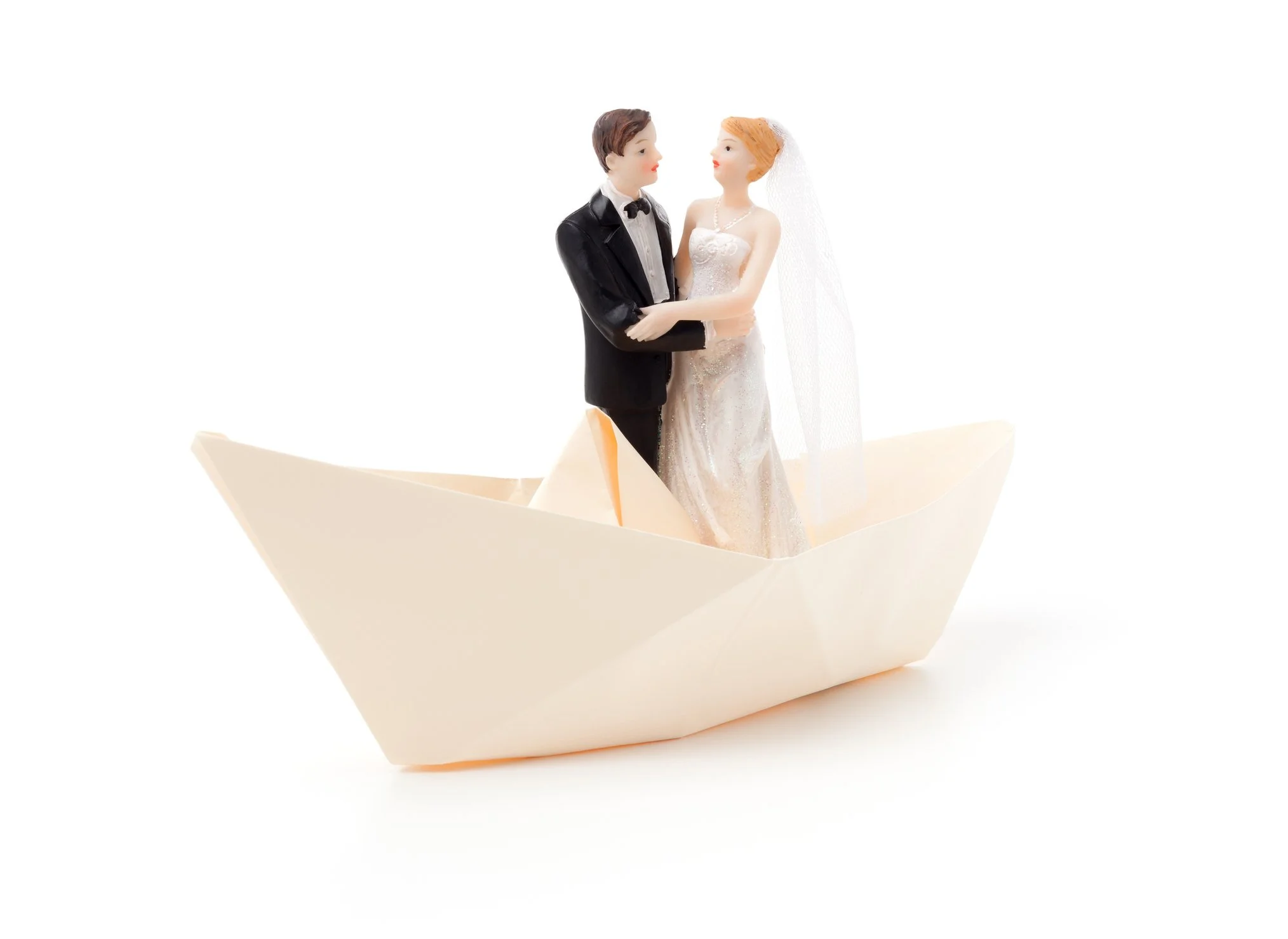 Wedding cake toppers shaped like a bride and groom standing in a paper boat.