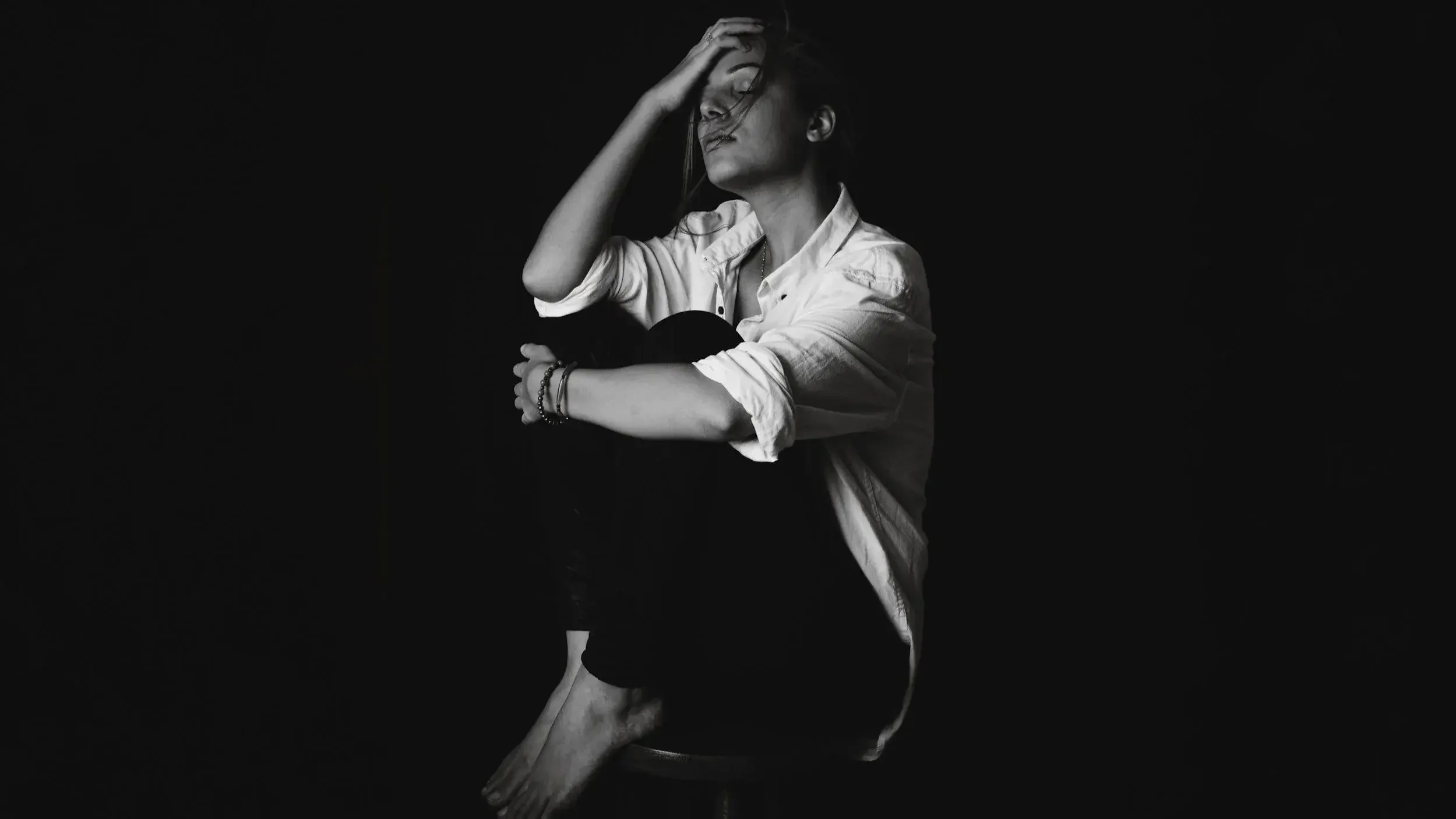 Lady with head in hands on a black background, symbolising separation anxiety struggles