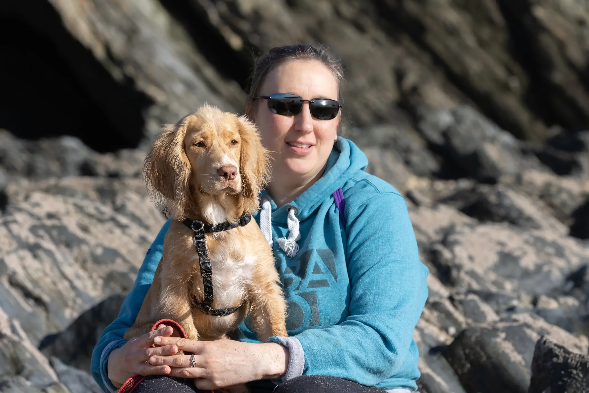 A woman holding a blonde spaniel puppy while sitting on rocky terrain, capturing the calm connection central to her separation anxiety support.