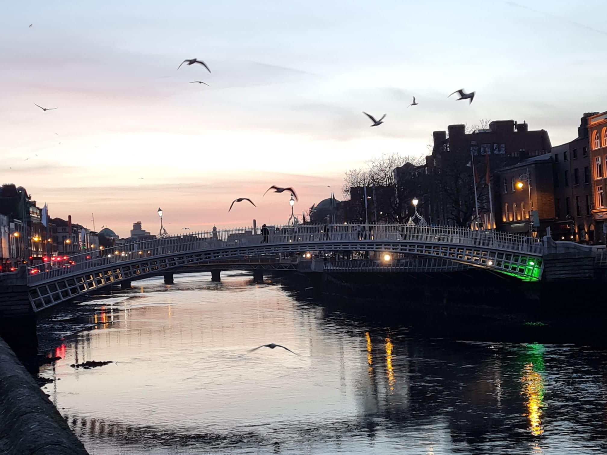 Dublin at sunset, birds flying, people walking on H'penny bridge Dublin