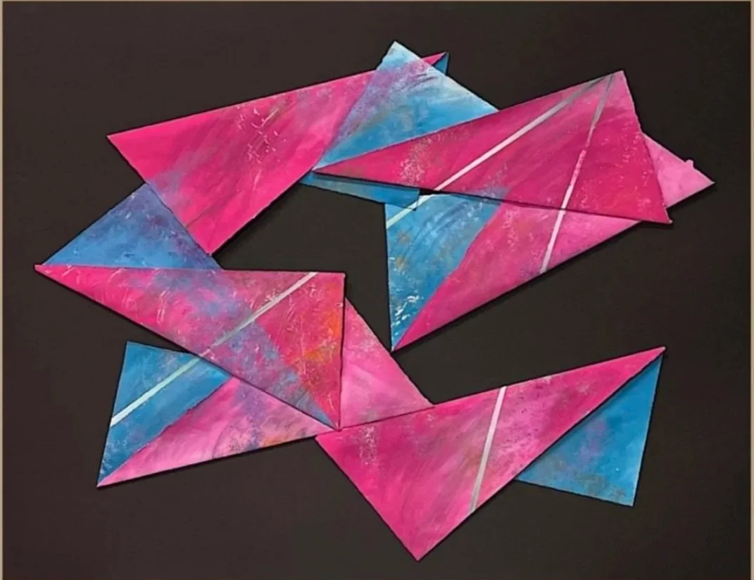 Colorful geometric paper art with pink and blue painted triangular shapes on a black background.