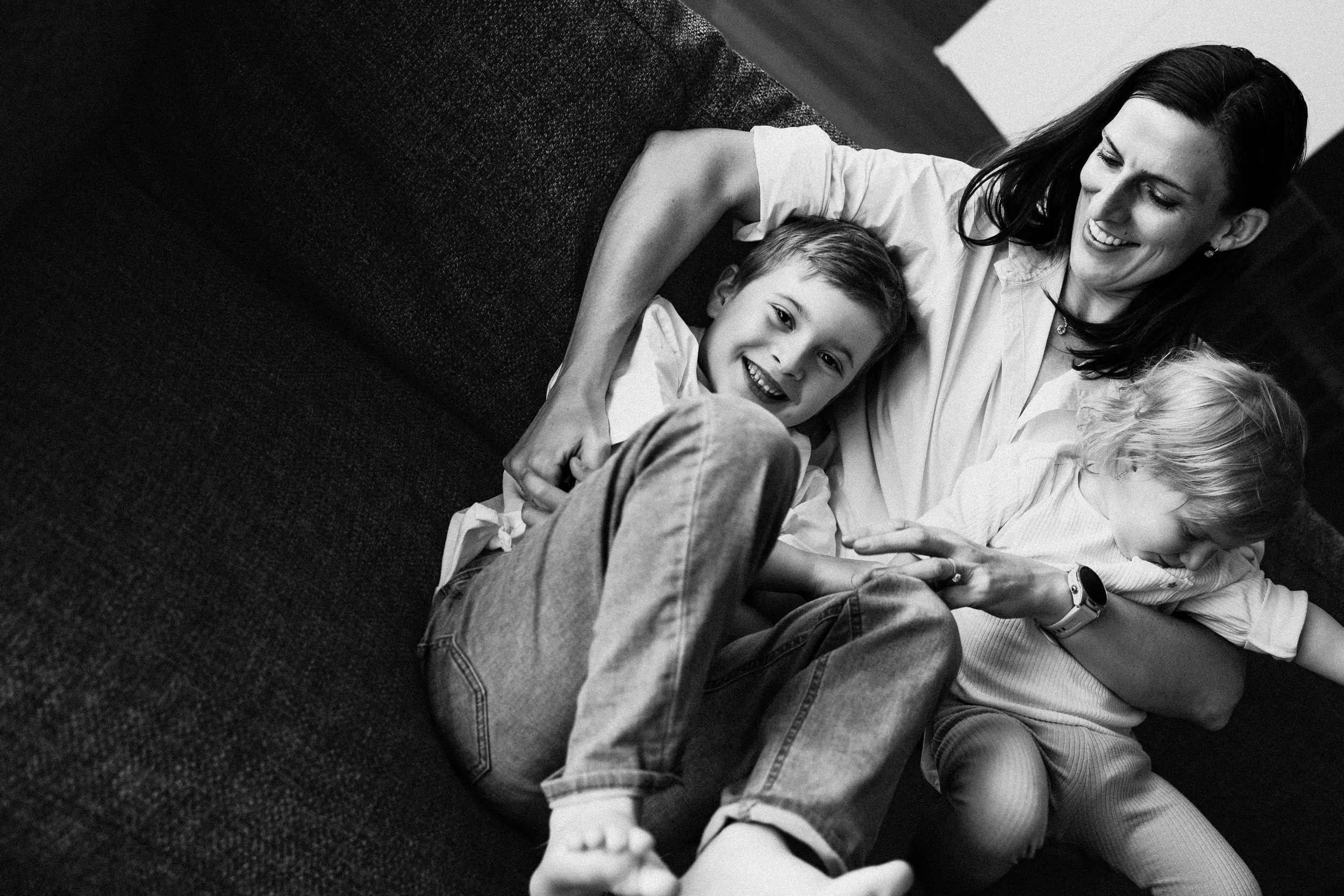 Black and white photo of a woman laughing with two children, one boy and one girl, on a couch.
