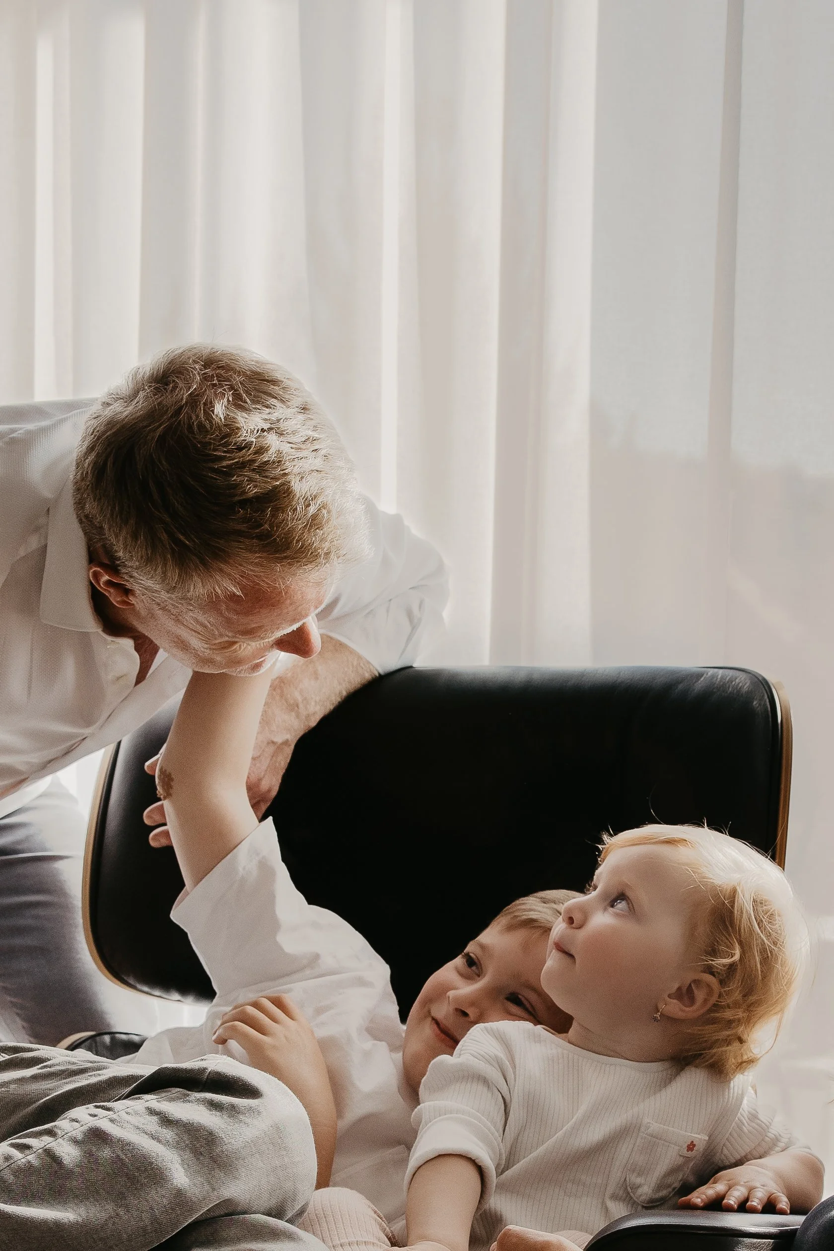 A grandfather lying on the floor with two young children, smiling and engaging in a playful moment.