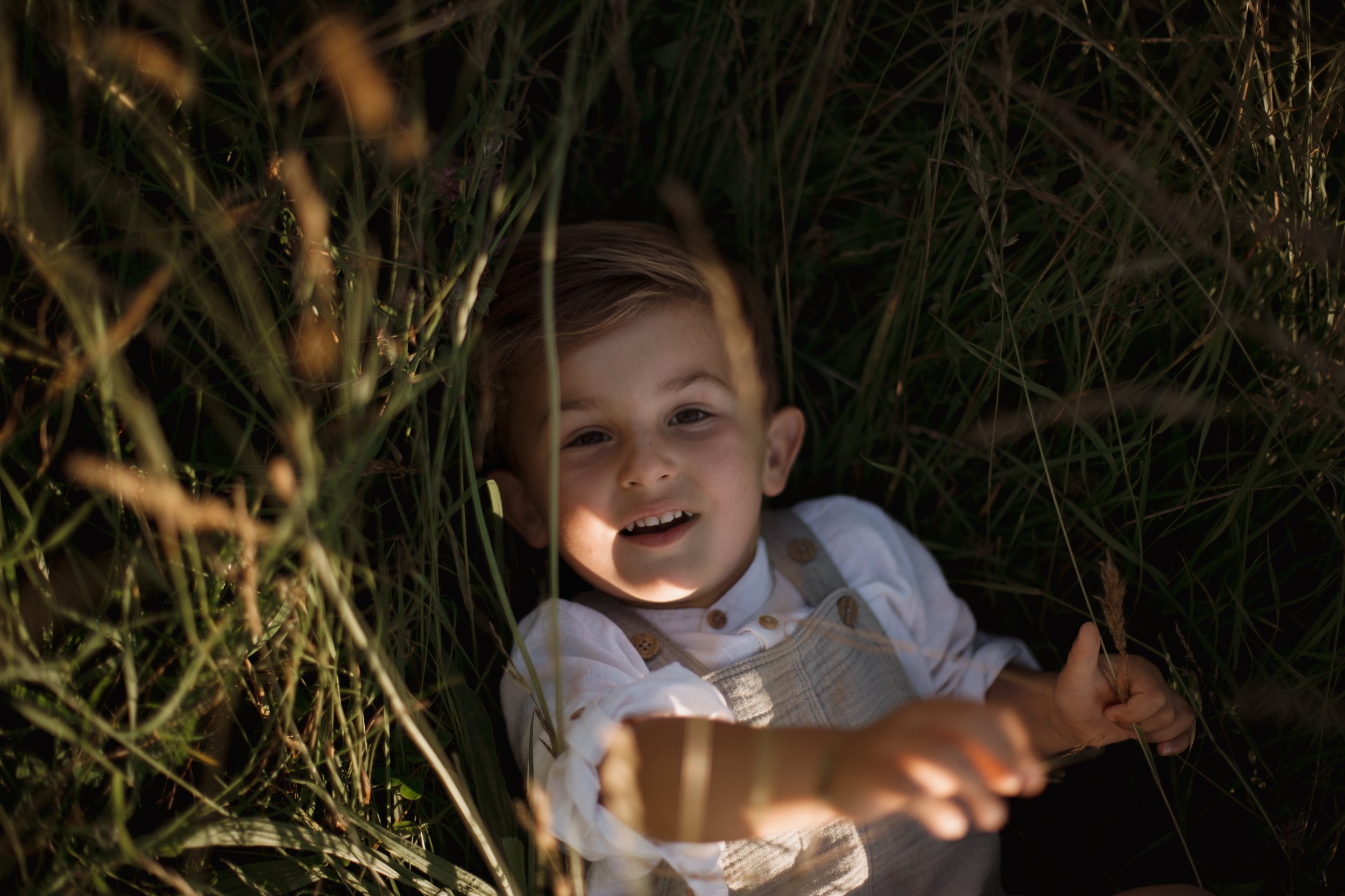close up of a kid slouching on a stool in a long belted khaki jacket