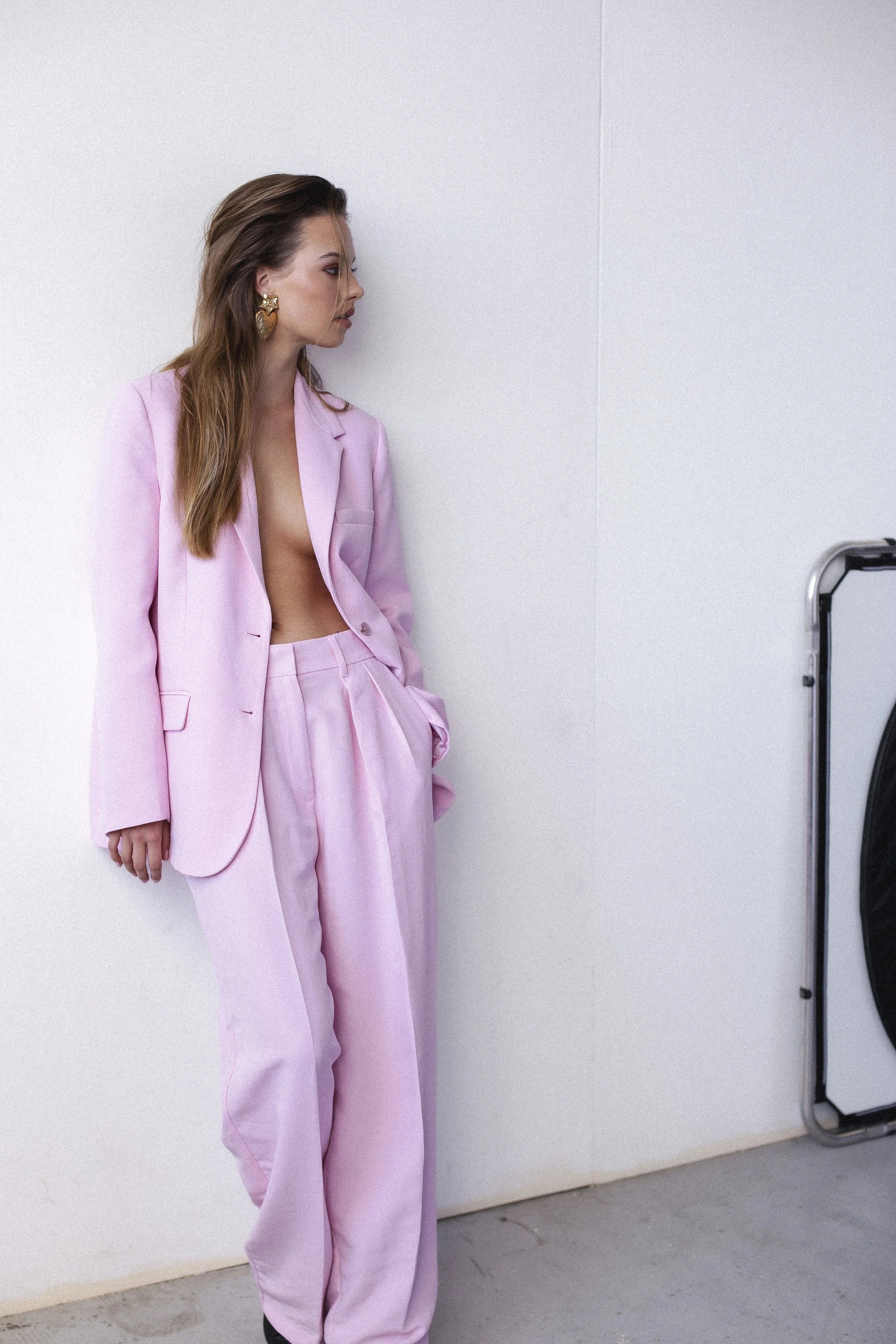 A woman in a pink suit with no shirt standing against a white wall, looking to the side.