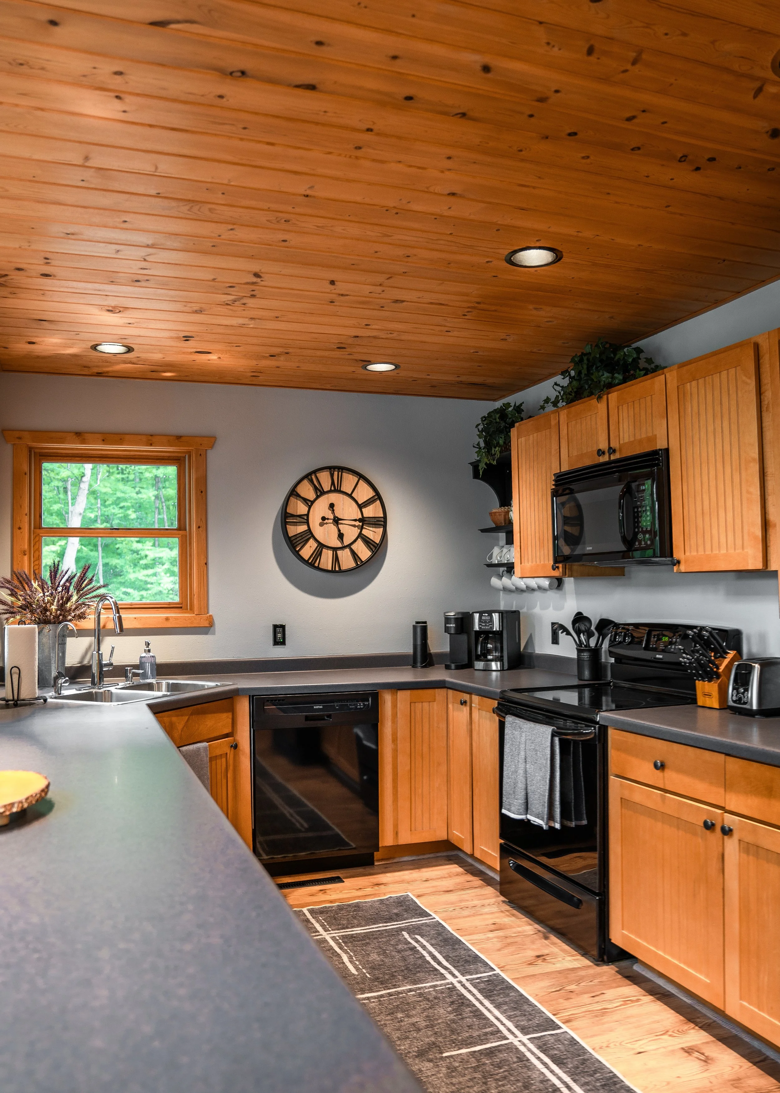 Kitchen with wooden cabinets, black appliances, a window with greenery outside, and a wooden ceiling.