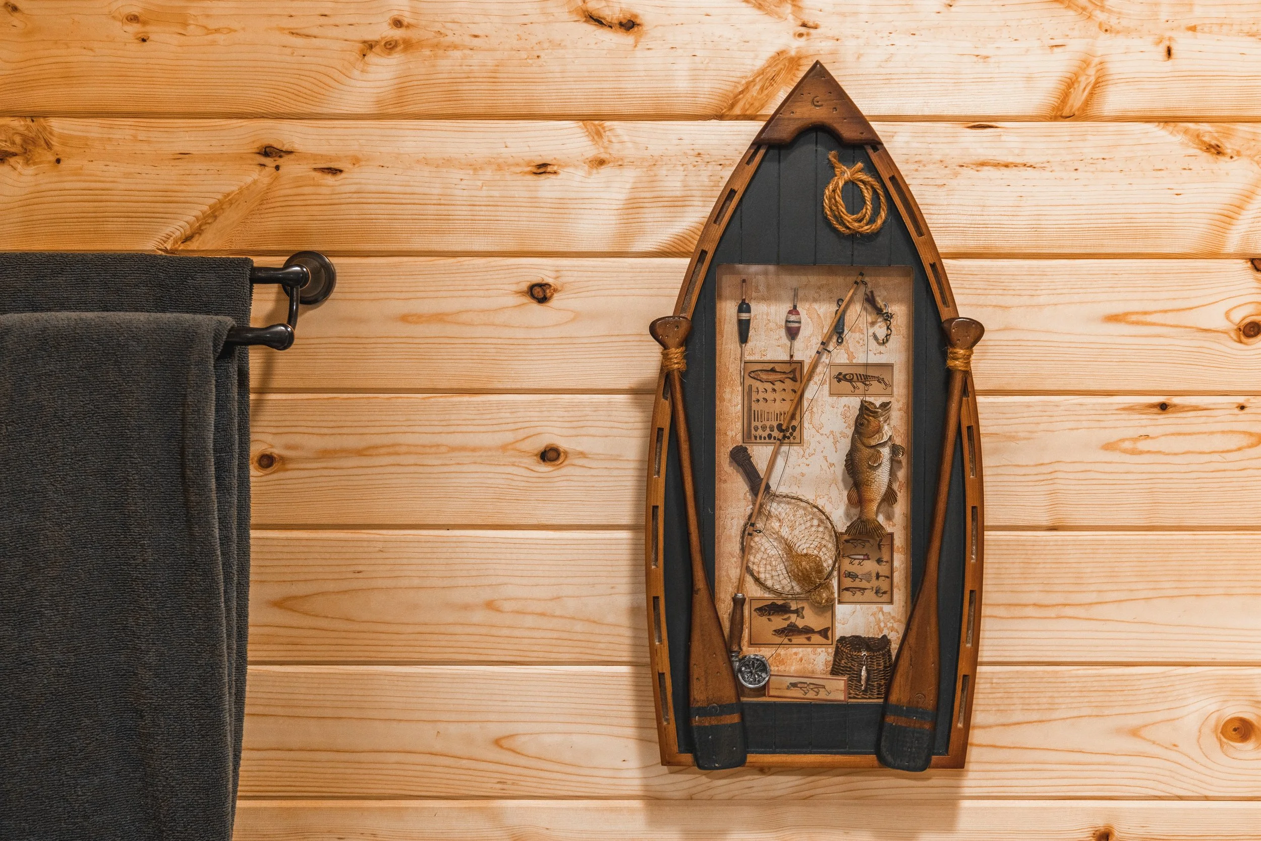 Decorative fishing boat wall hanging with fishing gear and novelty items on a wooden wall.