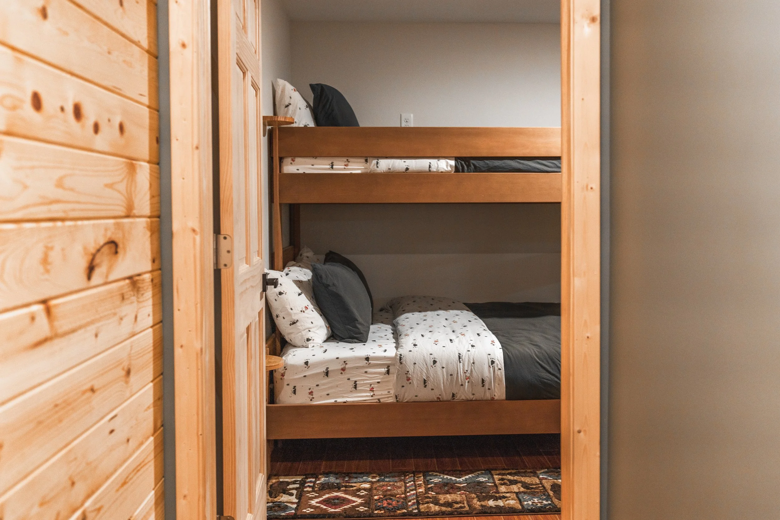 Bunk bed with black and white bedding and pillows in a cozy room with wooden walls and a patterned rug.