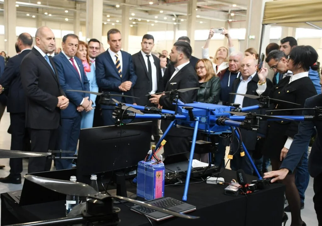 Group of people in business attire gathered around large drone at technology exhibition, several taking photos.