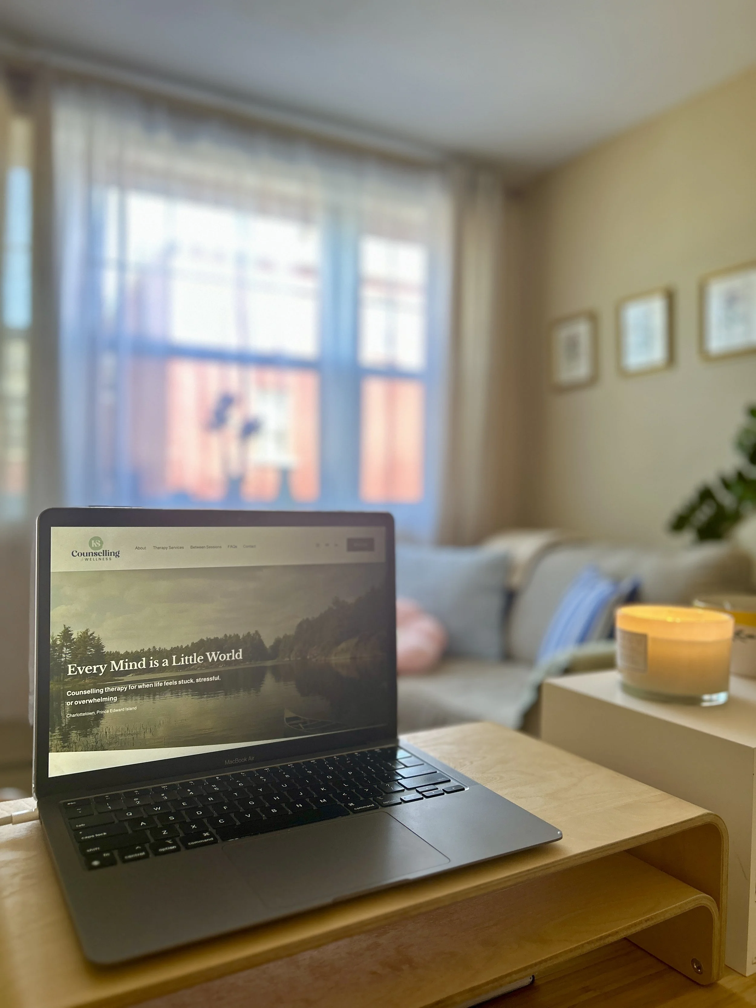 Laptop with KS Counselling & Wellness Website open, candle, office in the background