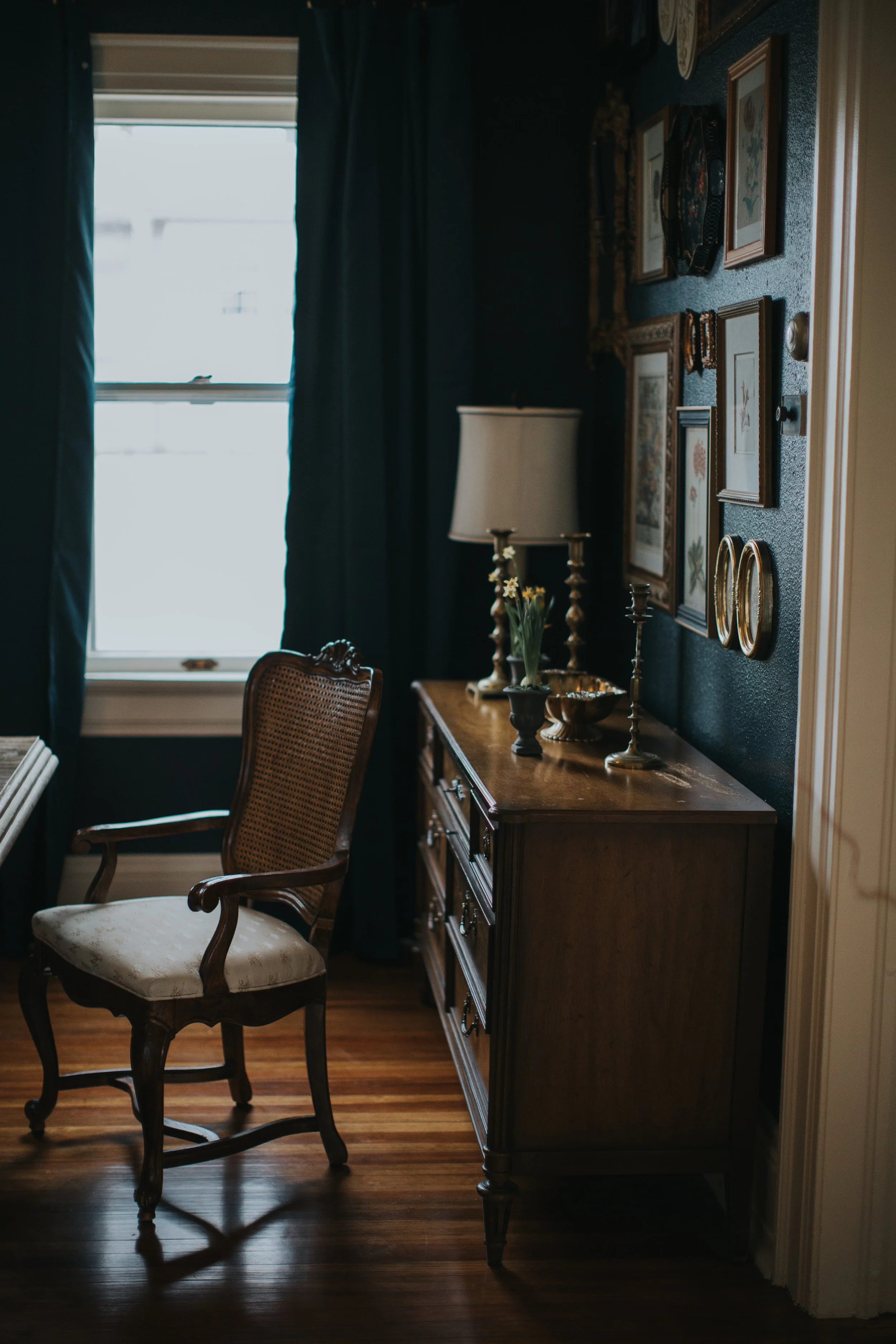 Antique cane-back chair beside a wood sideboard and layered gallery wall in a dark blue dining room.