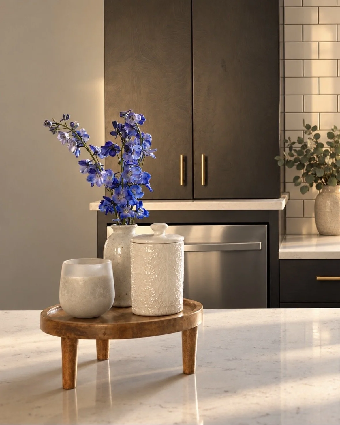Blue floral branch and three textured ceramic vases arranged on a round wood table beside a white tile wall.