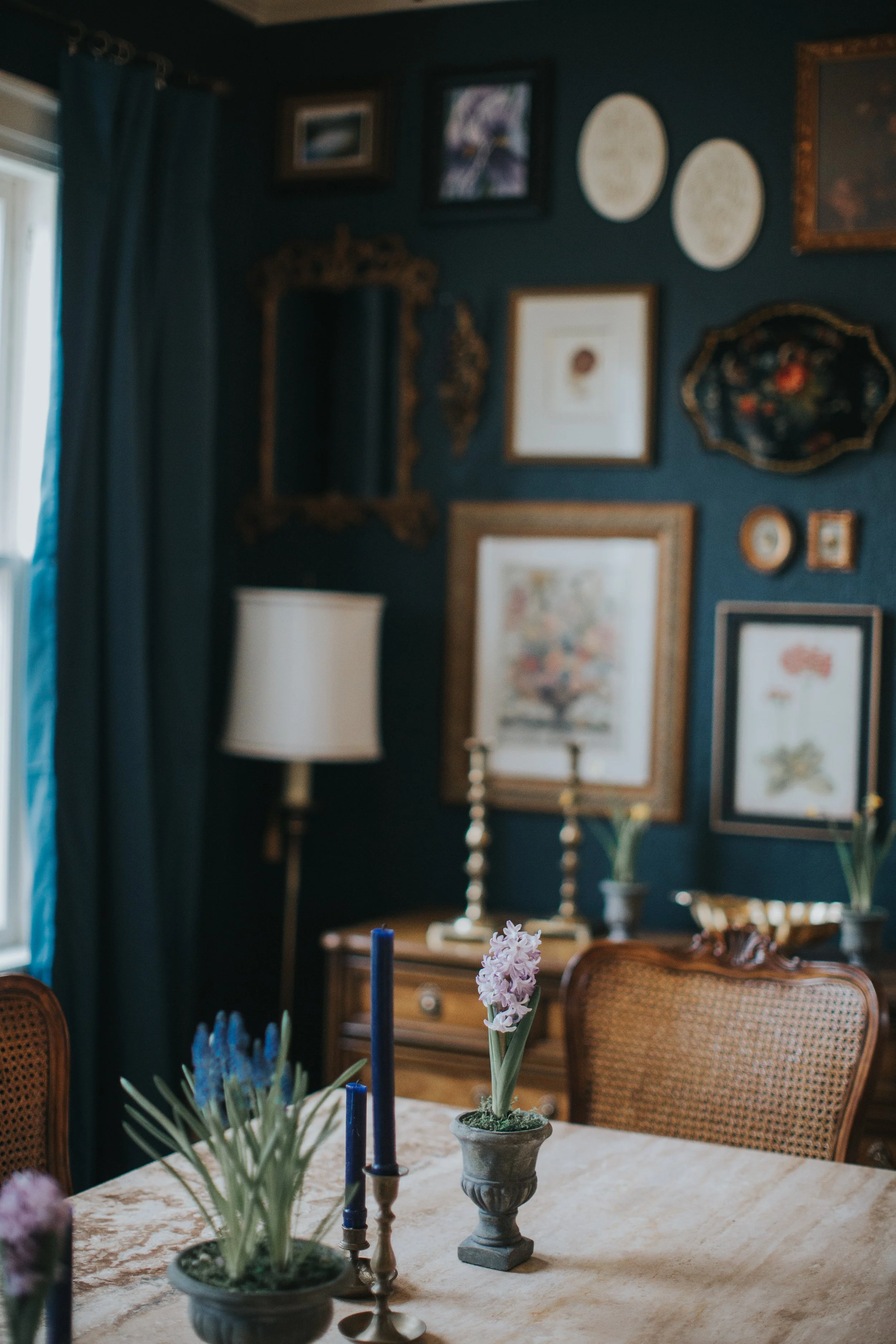 Antique cane-back chair beside a wood sideboard and layered gallery wall in a dark blue dining room.
