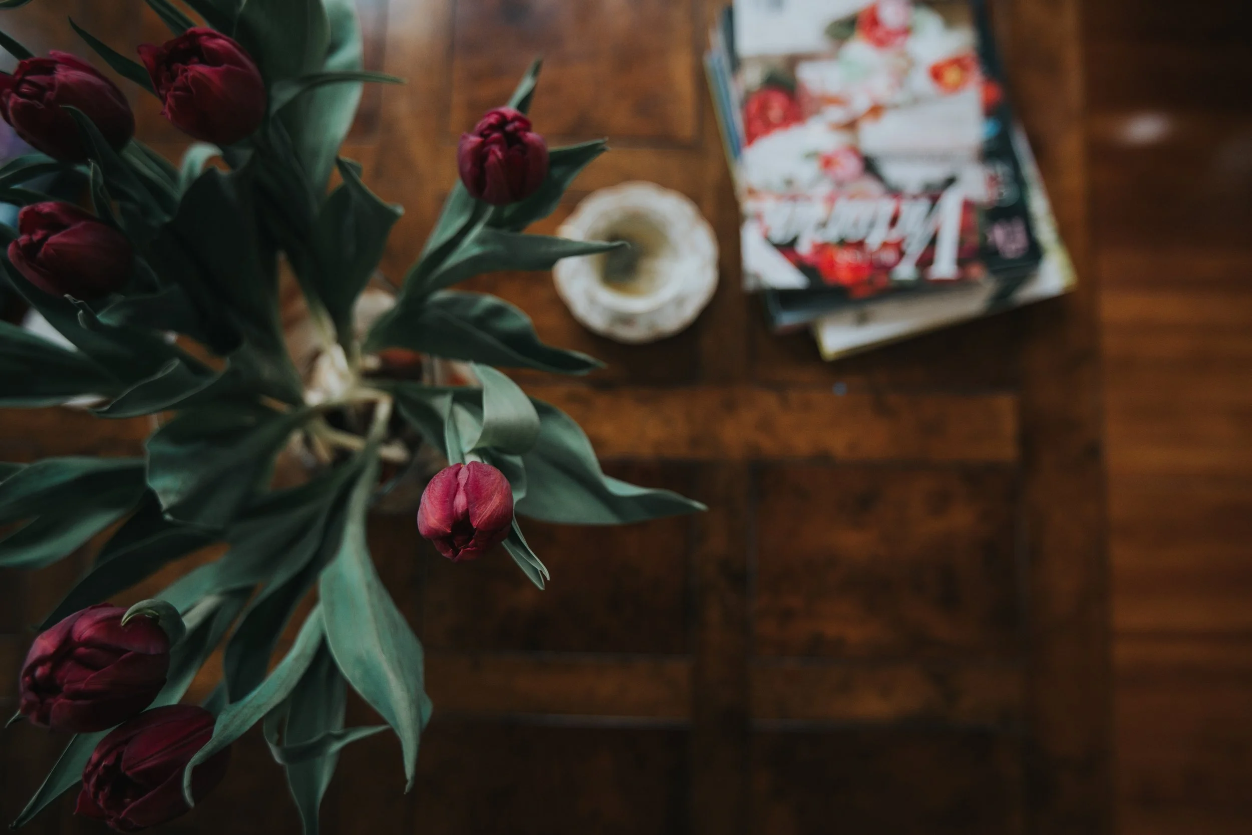 Close-up of deep red flowers, a carved stone bowl, and books arranged on an antique wood table.