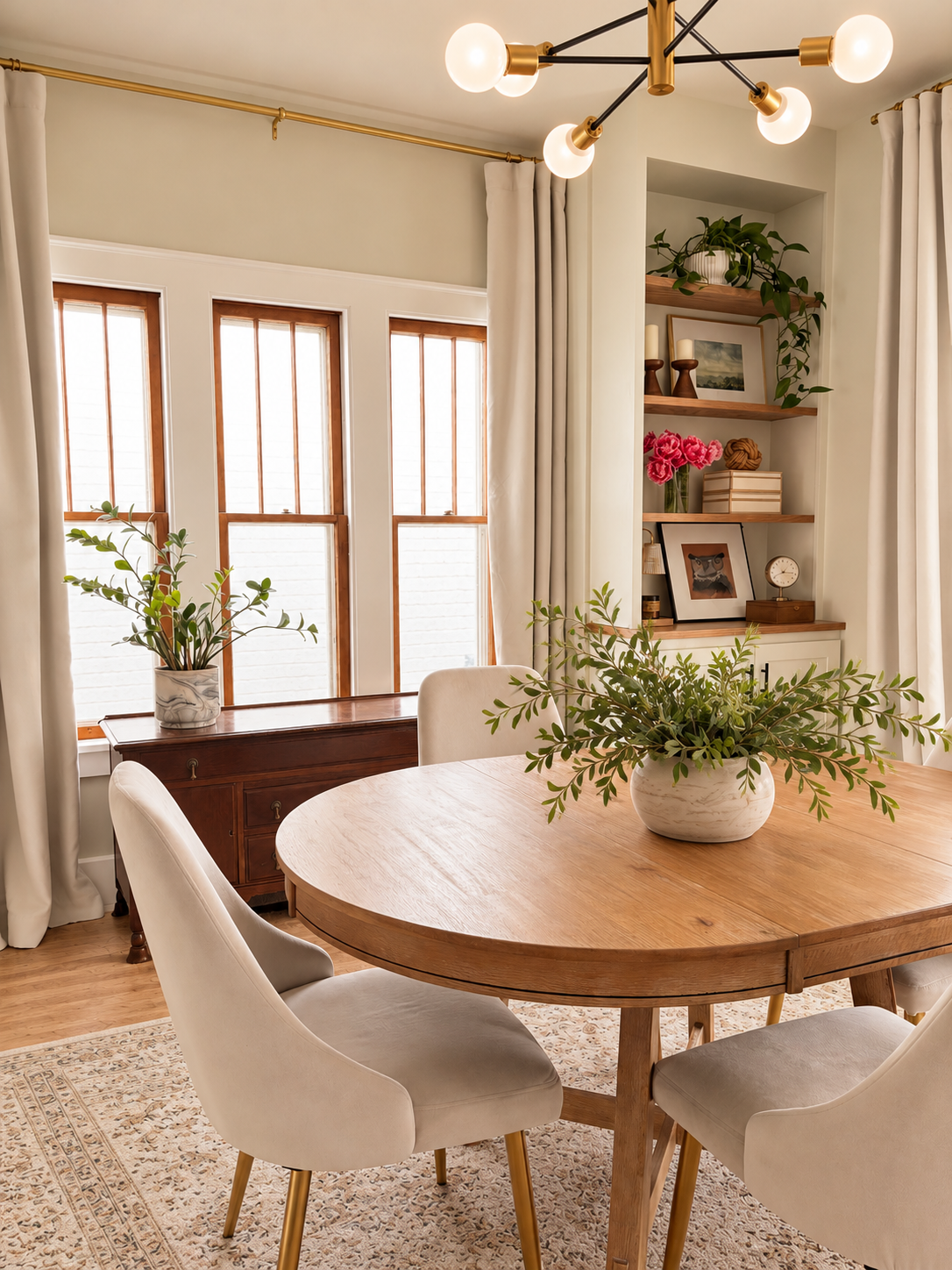 Neutral dining room with a round wood table, upholstered chairs, built-in shelves, and a modern branching chandelier.