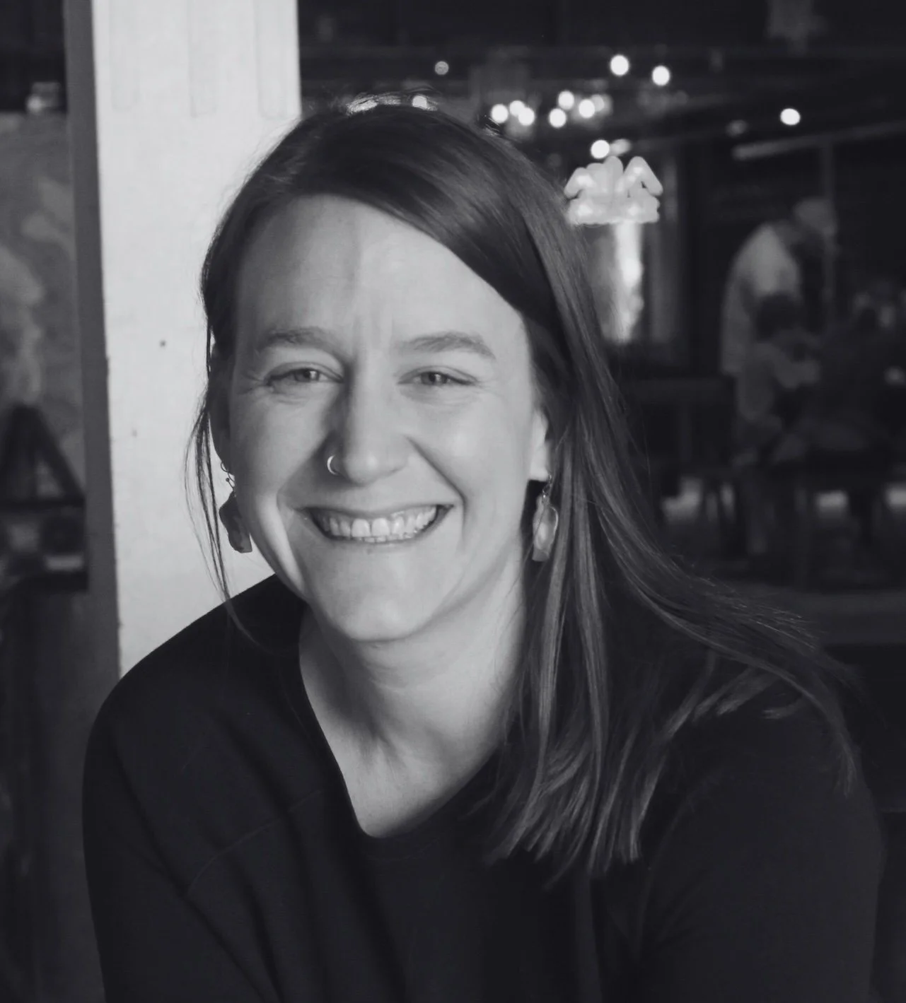 Woman with medium-length brown hair and a nose ring leans forward and smiles into camera