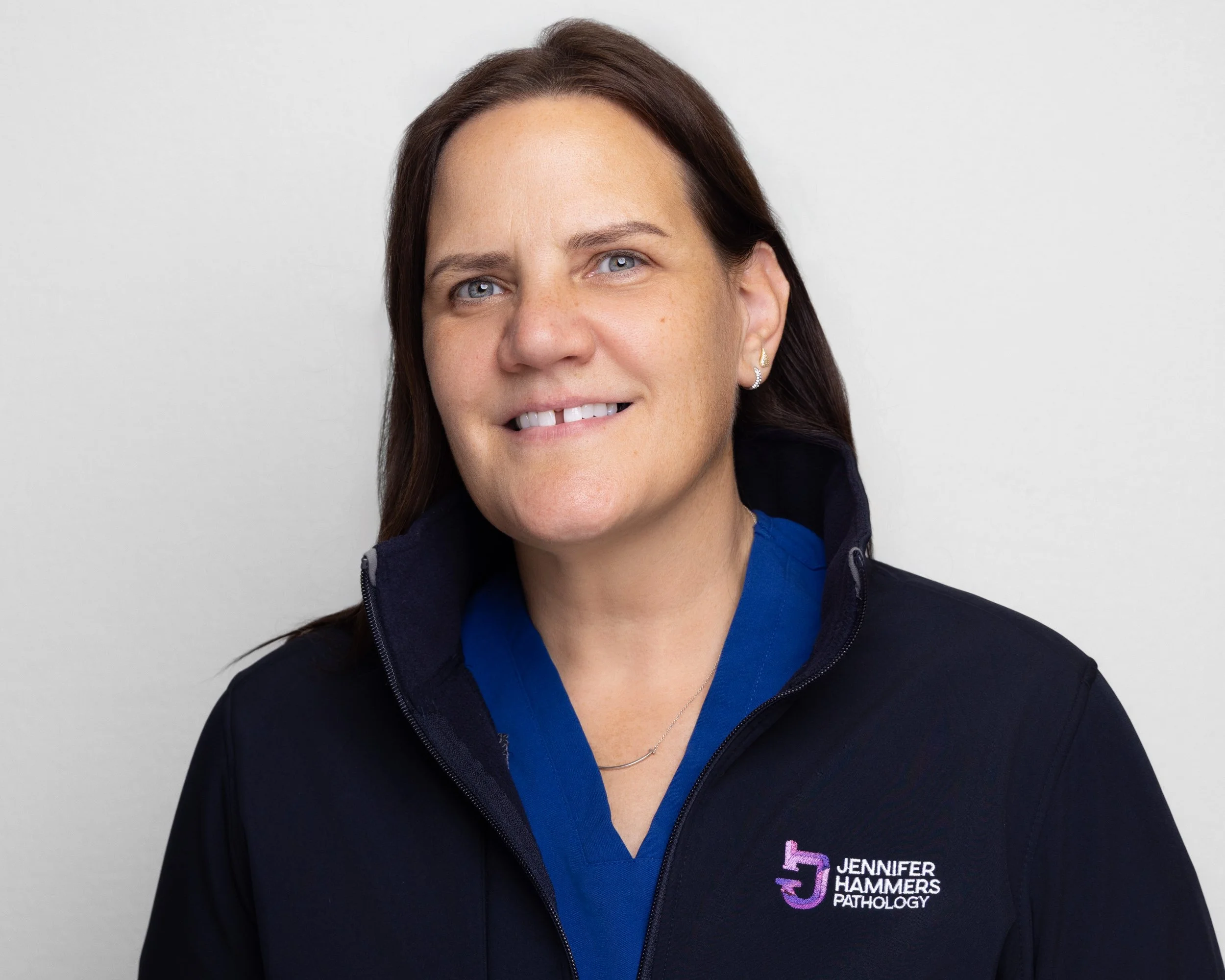 Portrait of Jennifer Hammers wearing a black jacket with her name and 'Pathology' embroidered on it, against a white background.