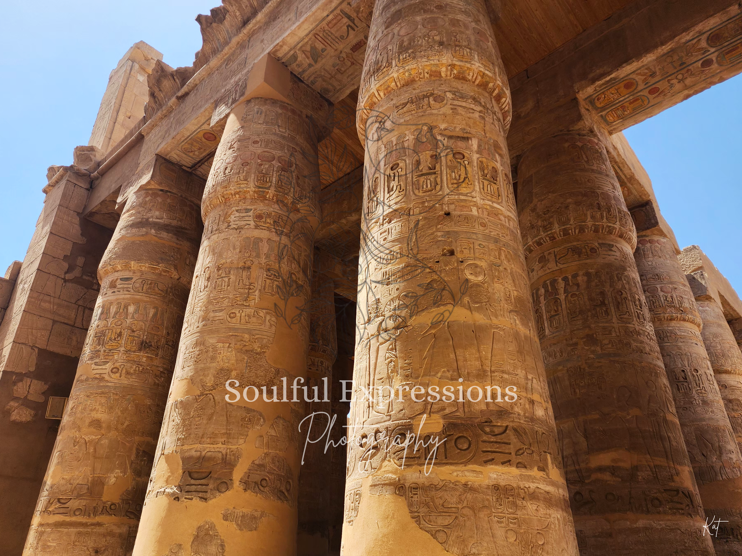 Ancient Egyptian stone columns with hieroglyphic carvings and faded colors, part of an ancient temple under a clear blue sky.
