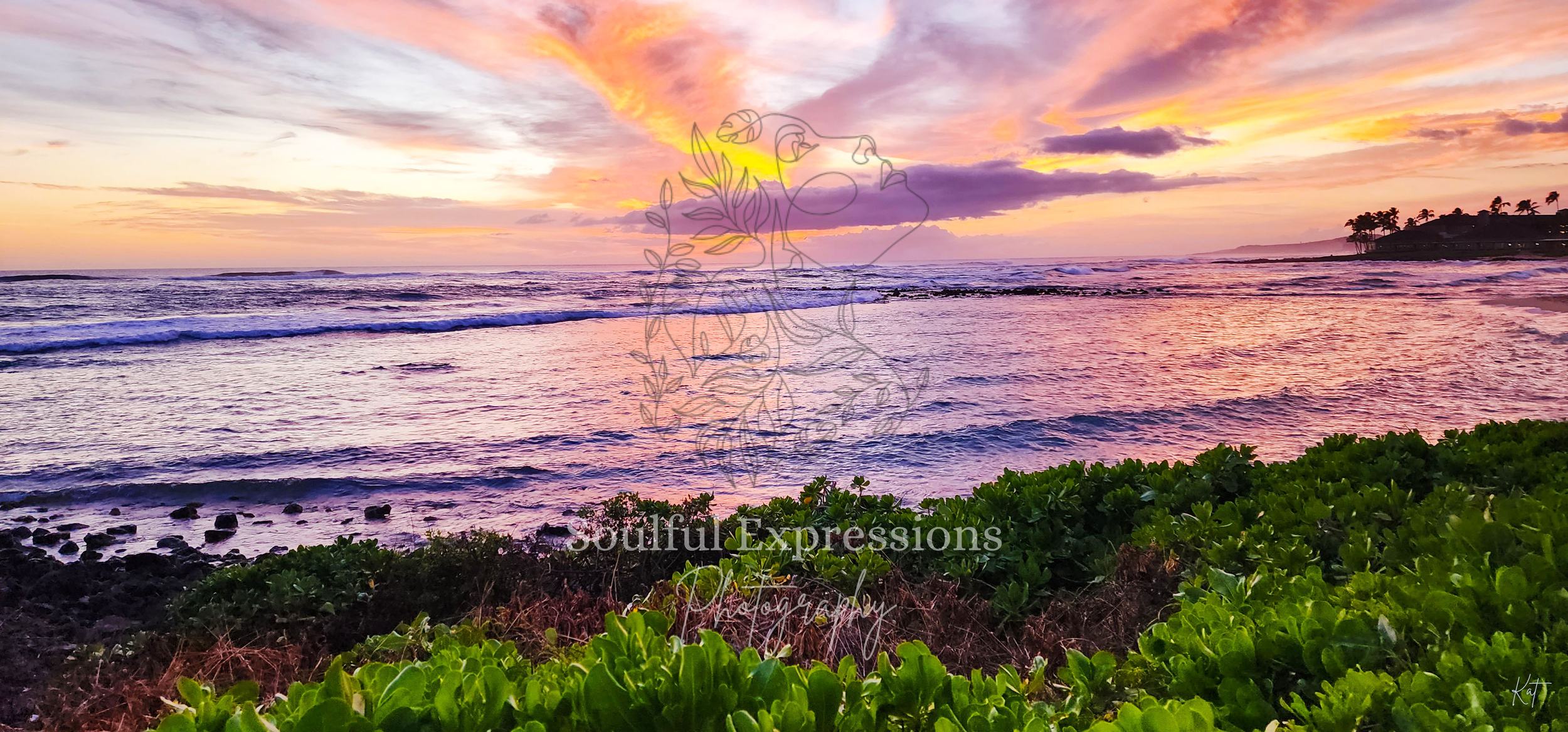 A vibrant sunset over the ocean with pink, purple, and orange hues in the sky in Kauai, Hawaii. Green foliage covers the foreground with rocky shore rocks and gentle waves in the water.
