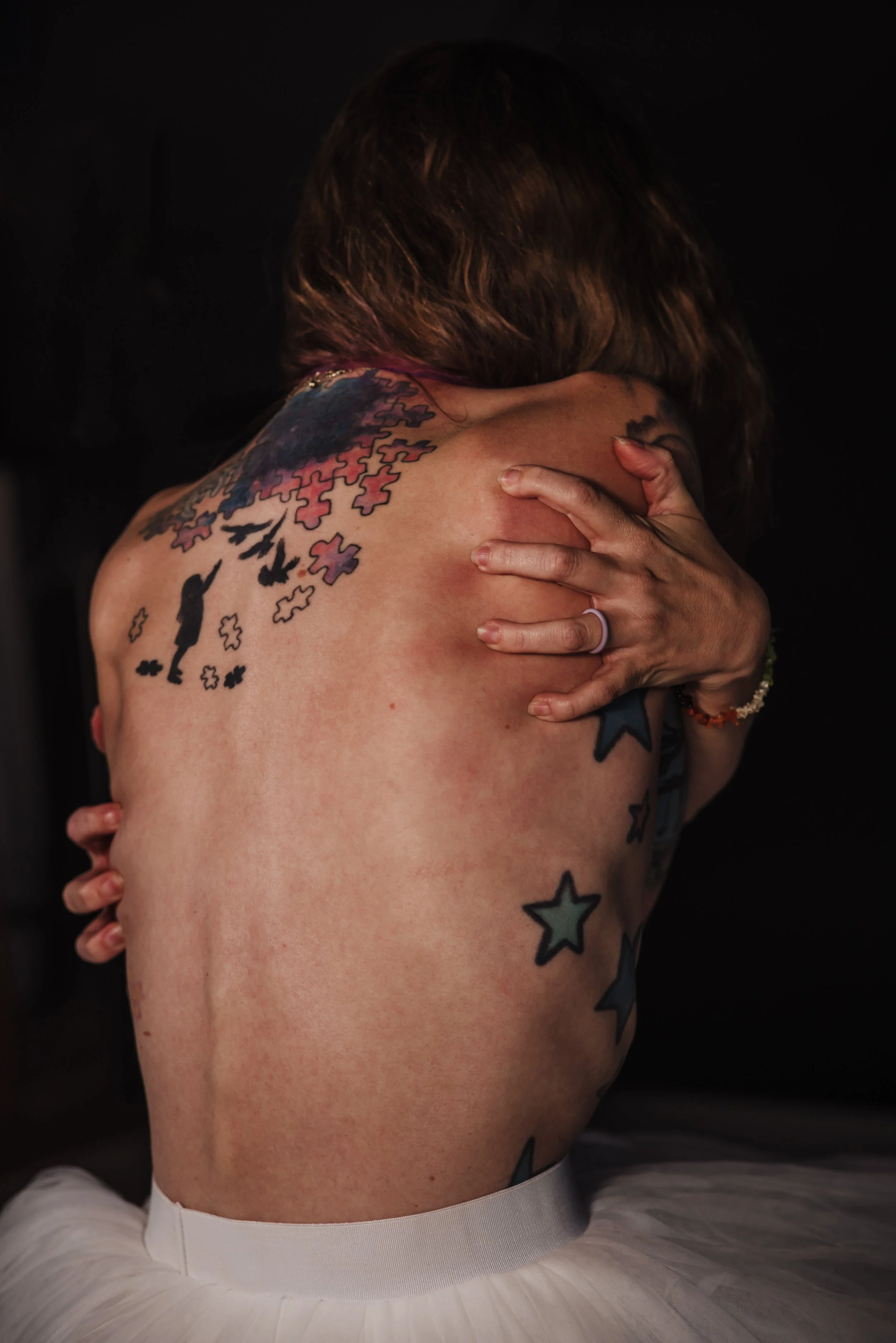 Introspective, moody photo of Kat Harrison embracing herself, illustrating self-compassion and healing through personal darkness.