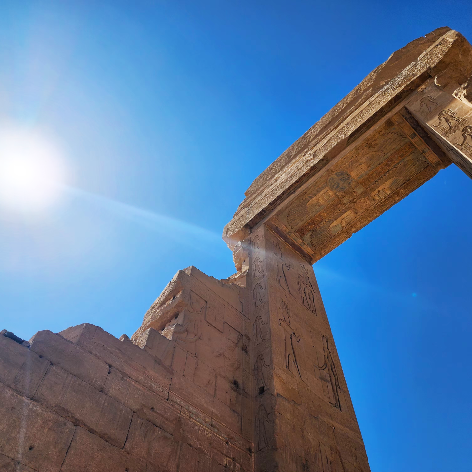 Ancient Egyptian stone monument with hieroglyphic carvings under a bright blue sky with the sun shining.