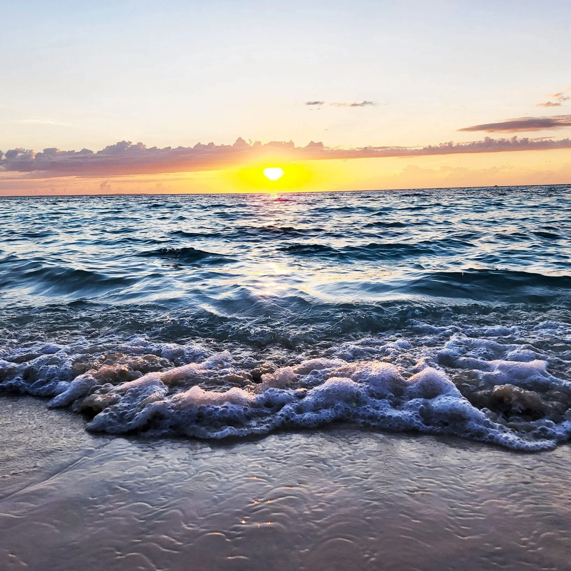 Sunset over the ocean with gentle waves and foam on sandy shore in Turks and Caicos.