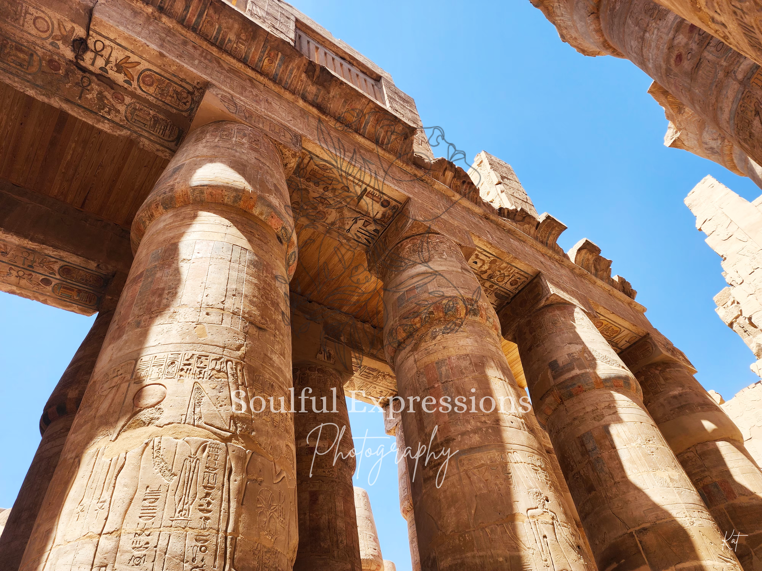 Ancient Egyptian temple columns with hieroglyphic carvings under a bright blue sky.