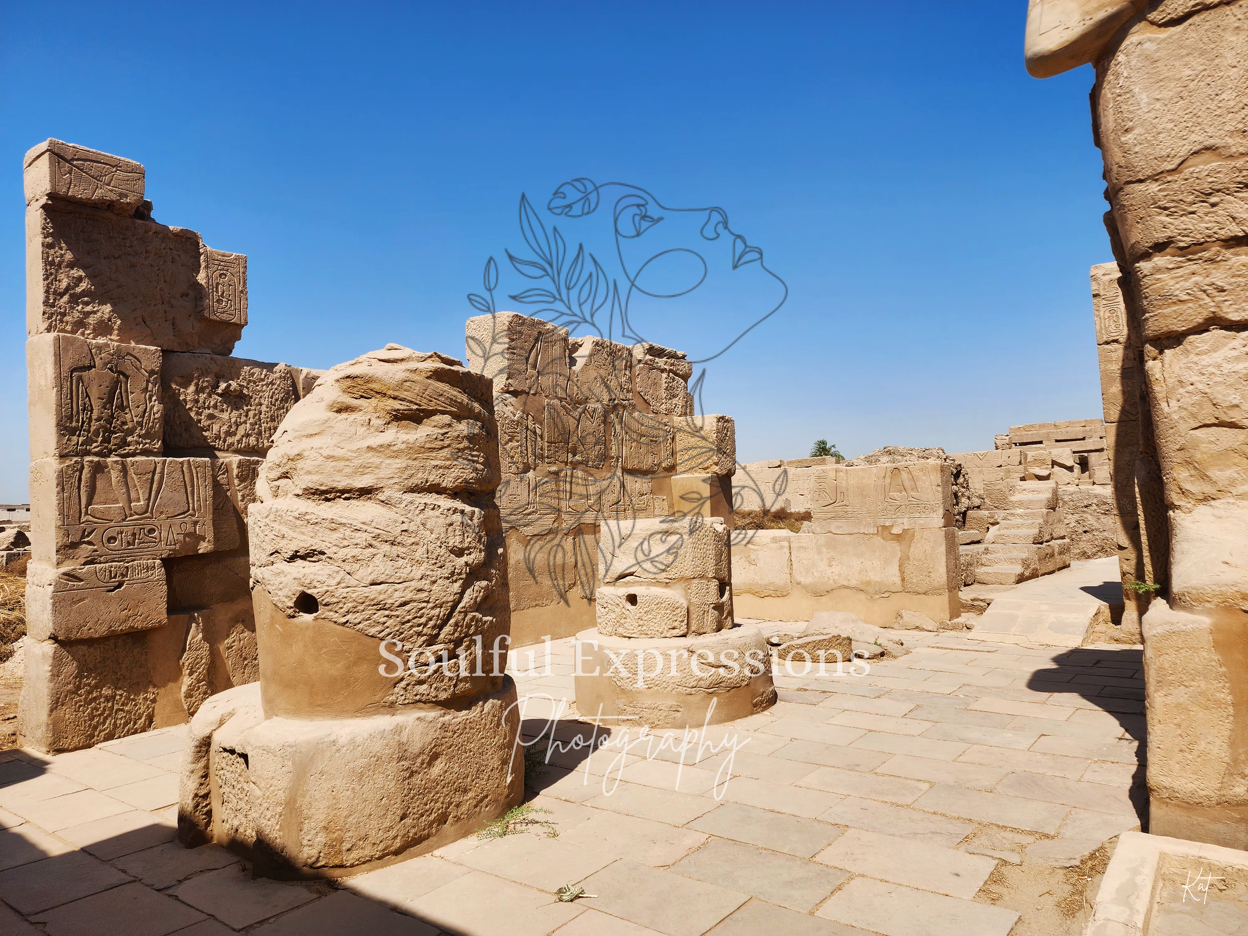 Ancient stone ruins with carved hieroglyphs and inscriptions, under a bright blue sky in Egypt.