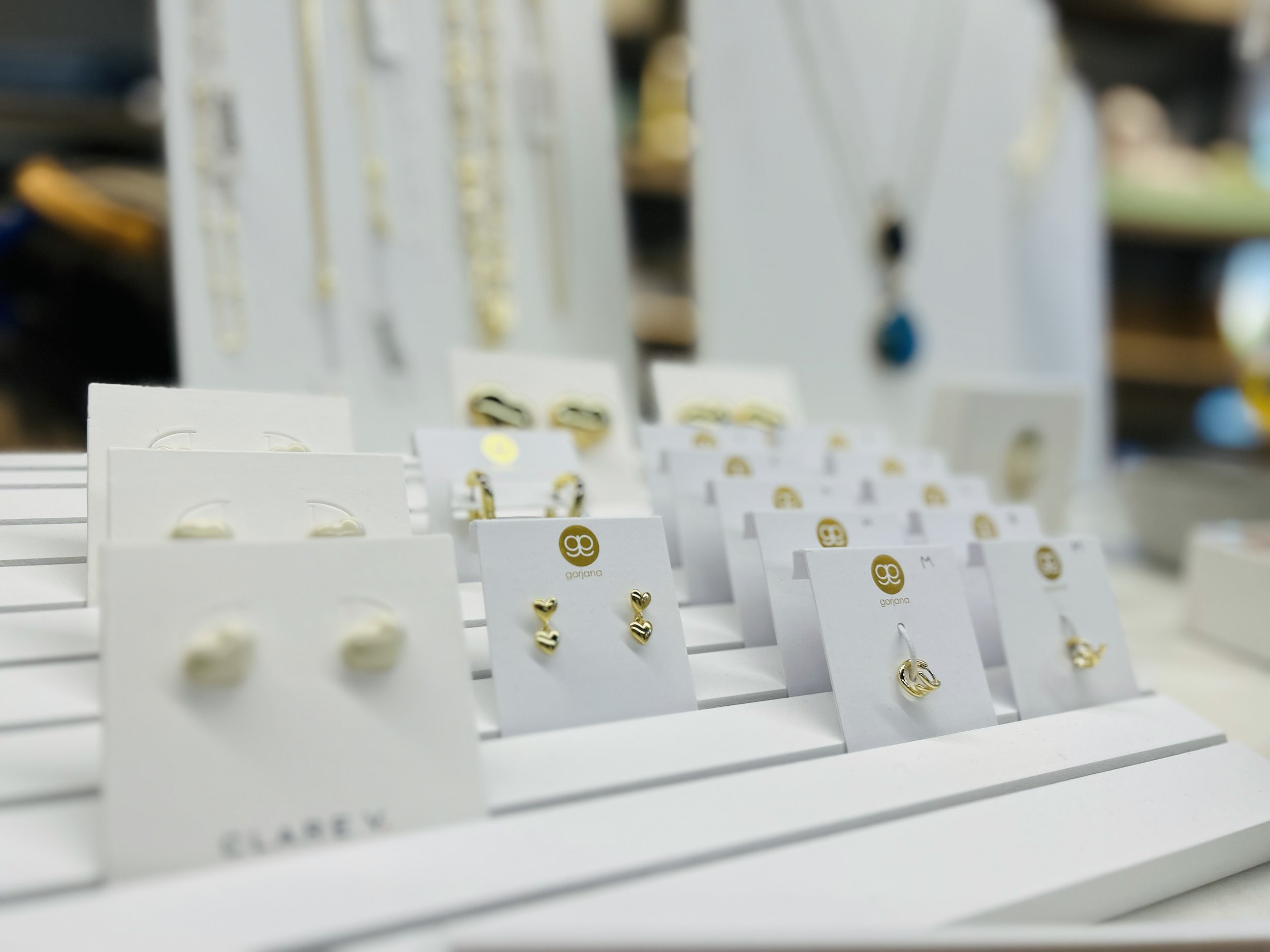 Display of gold jewelry, including earrings and rings, on white cards at a retail store.