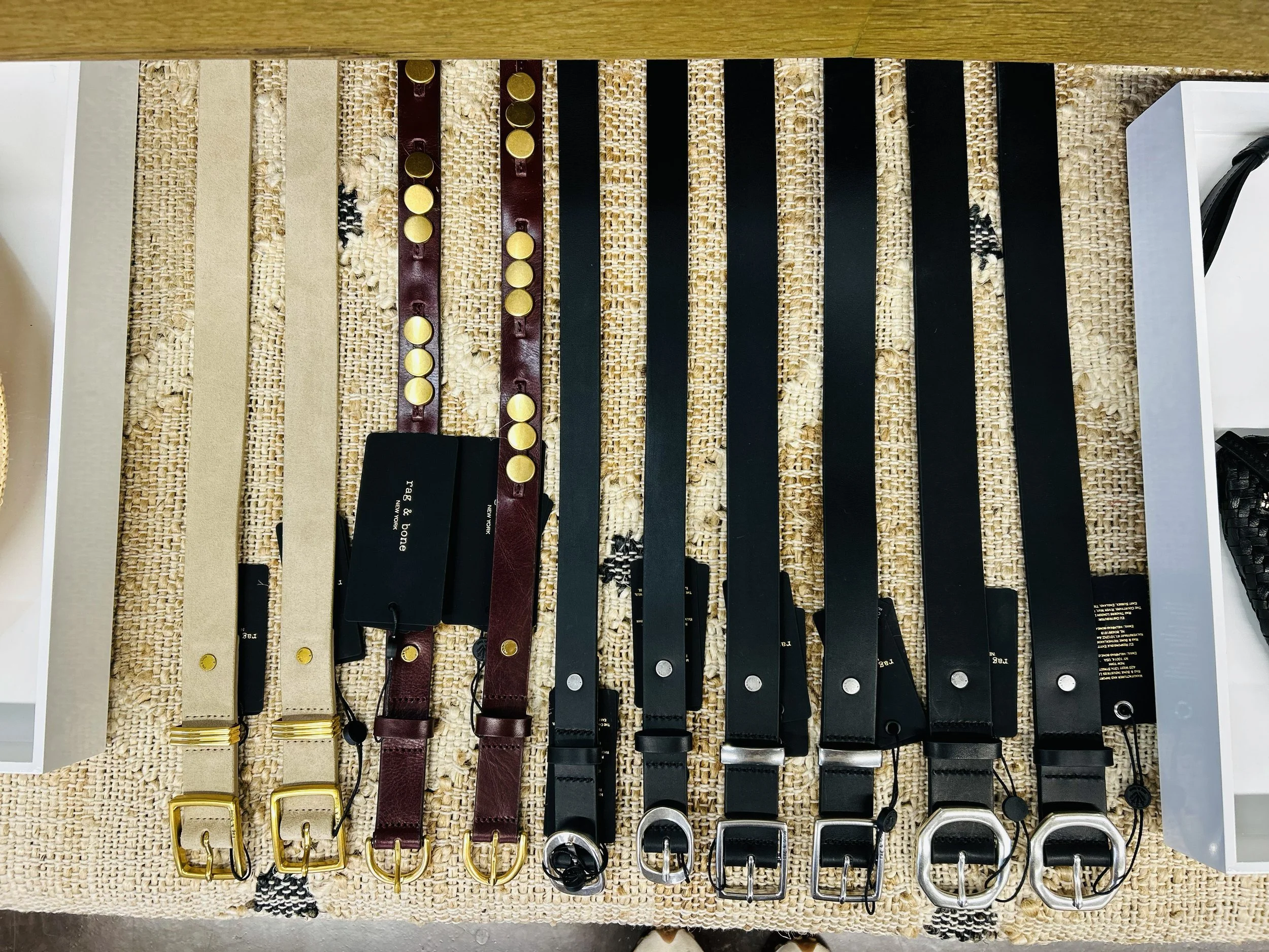 A collection of various belts laid out on a woven surface, featuring different colors and buckle styles.