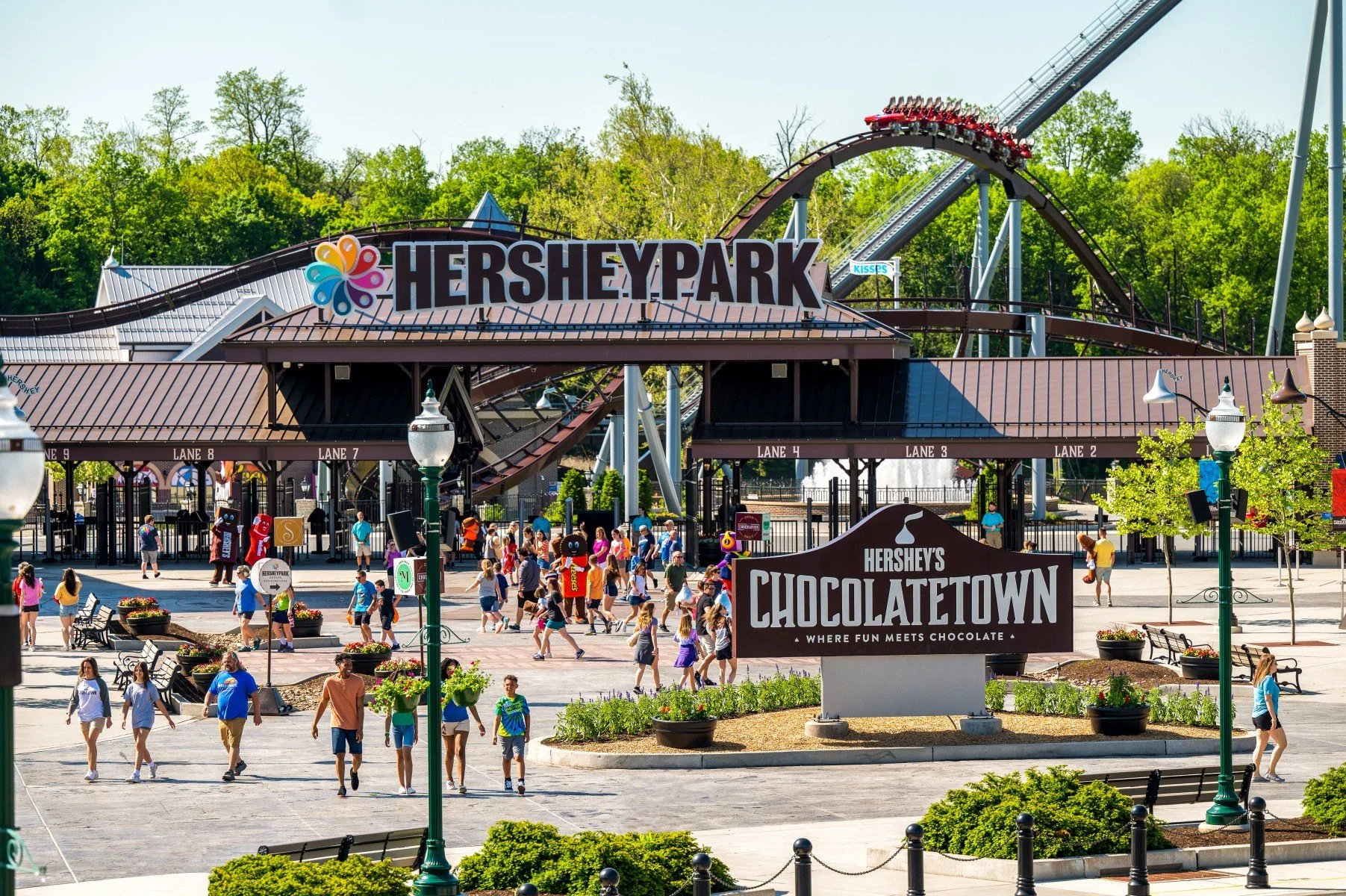 Entrance of Hersheypark with visitors and roller coaster in background.