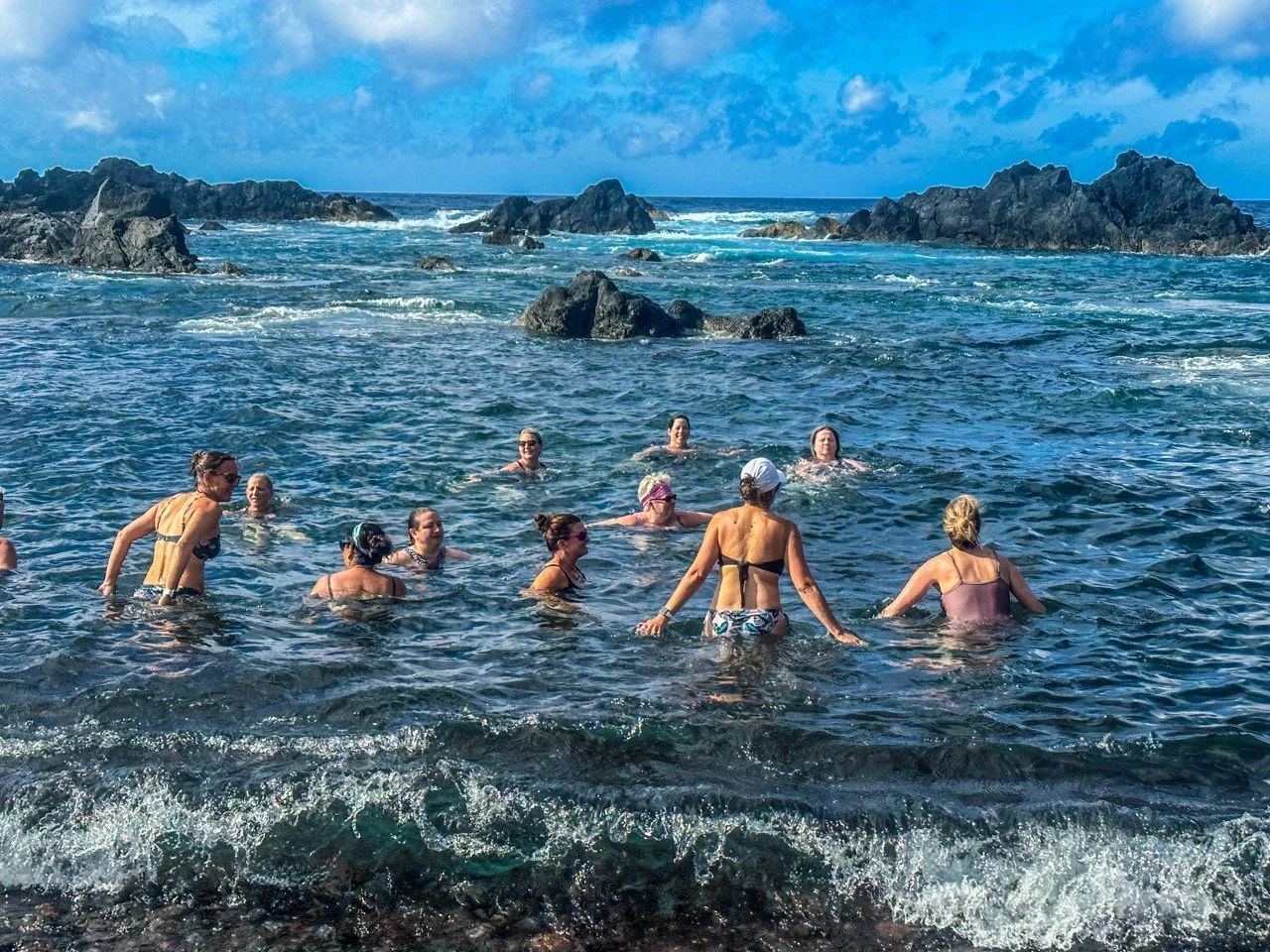 Group of people swimming in the sea near rocky coastline under blue sky.