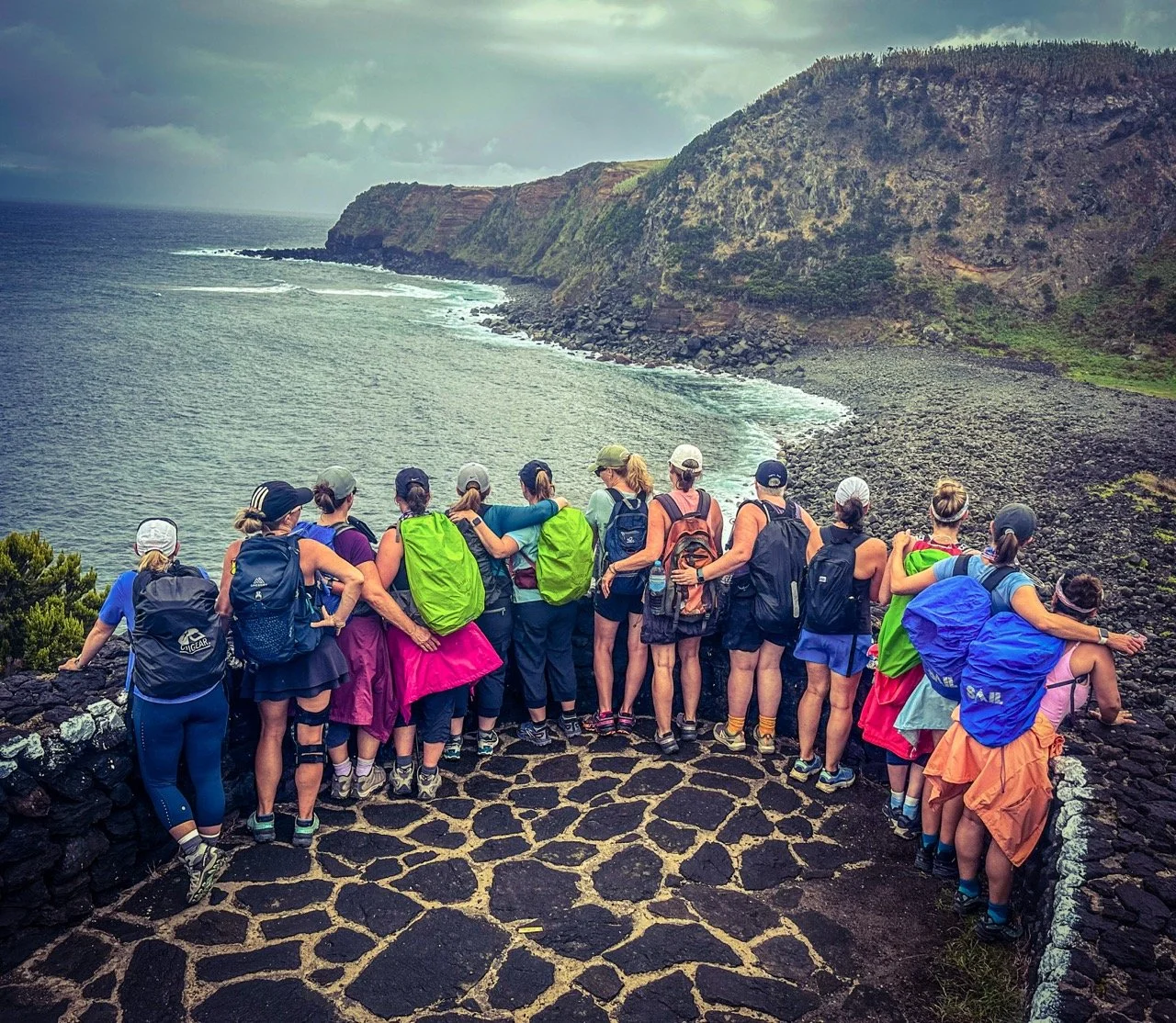 Group of hikers standing on rocky overlook, facing scenic coastline with cliffs and ocean.