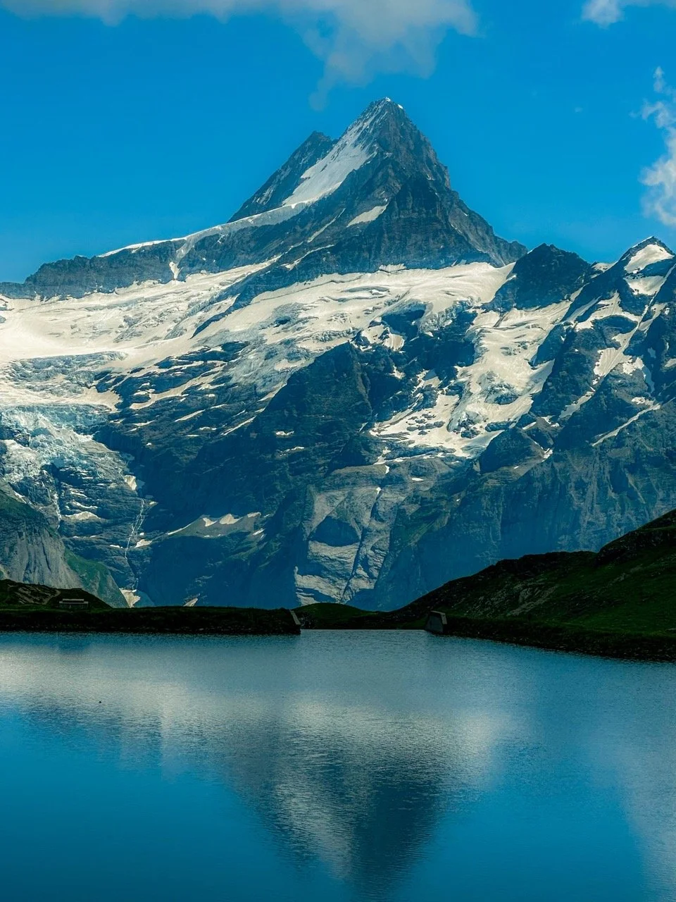Scenic mountain landscape with snow-covered peaks and a lake reflecting the mountain under a clear blue sky.