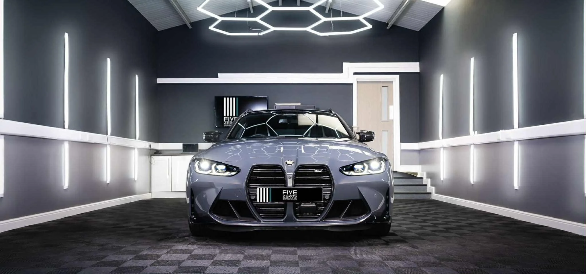 Gray BMW car in a modern, well-lit indoor showroom with dark walls and geometric ceiling lights.