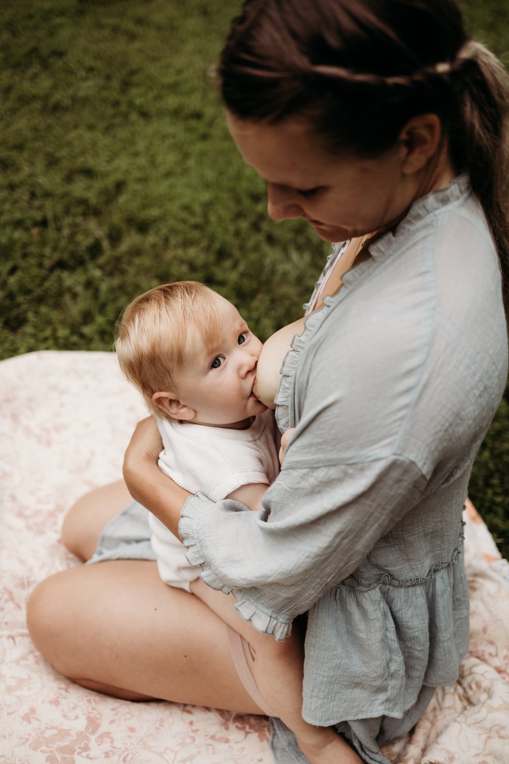 Mother breastfeeding a baby on a blanket outdoors