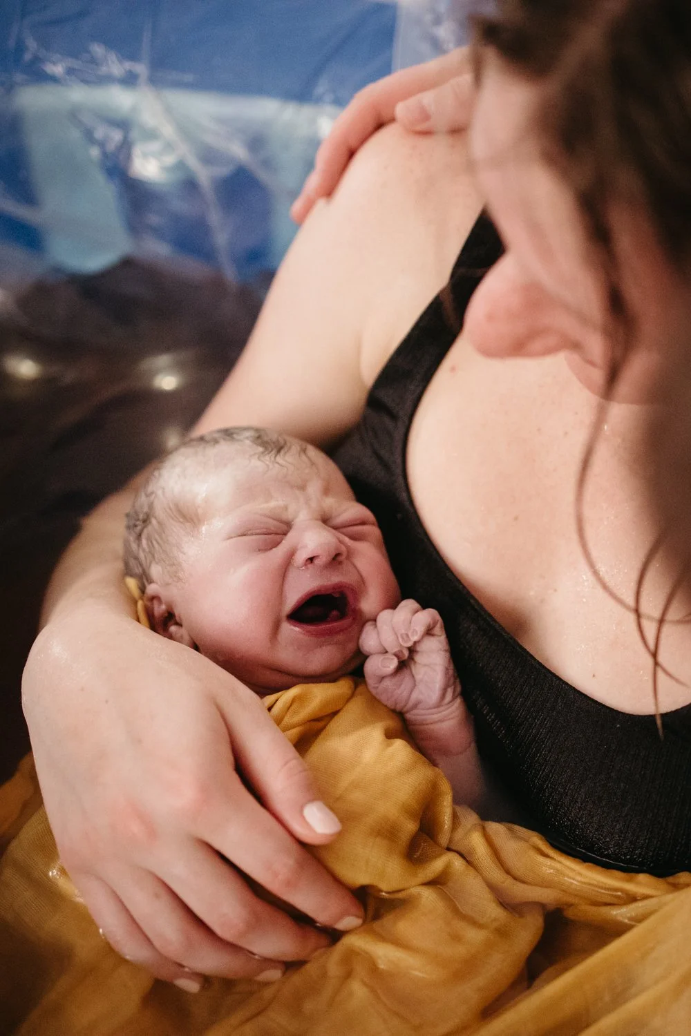 Mother holding newborn baby wrapped in yellow blanket during water birth.