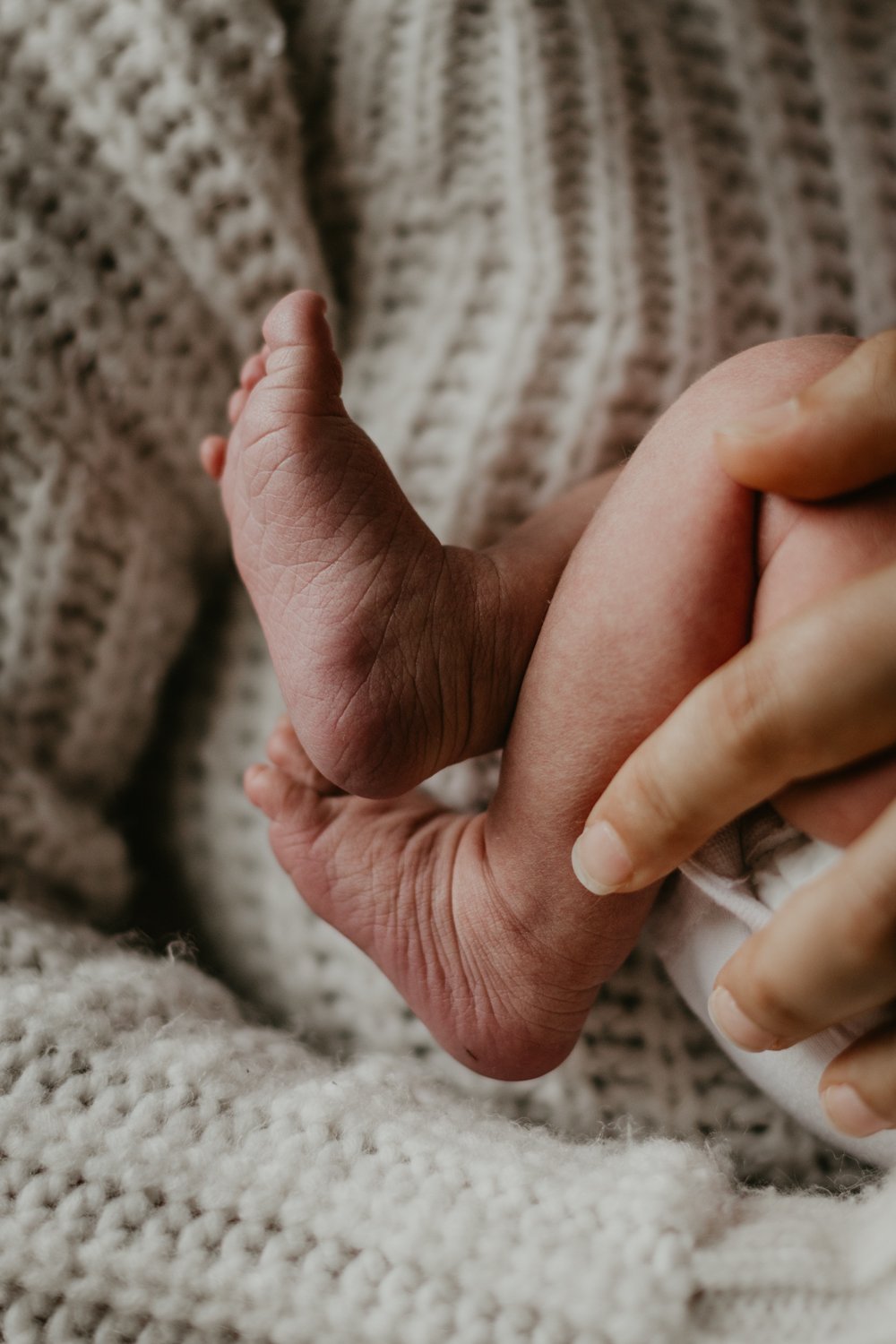 Close-up of a baby's feet and hands against a soft knitted blanket.