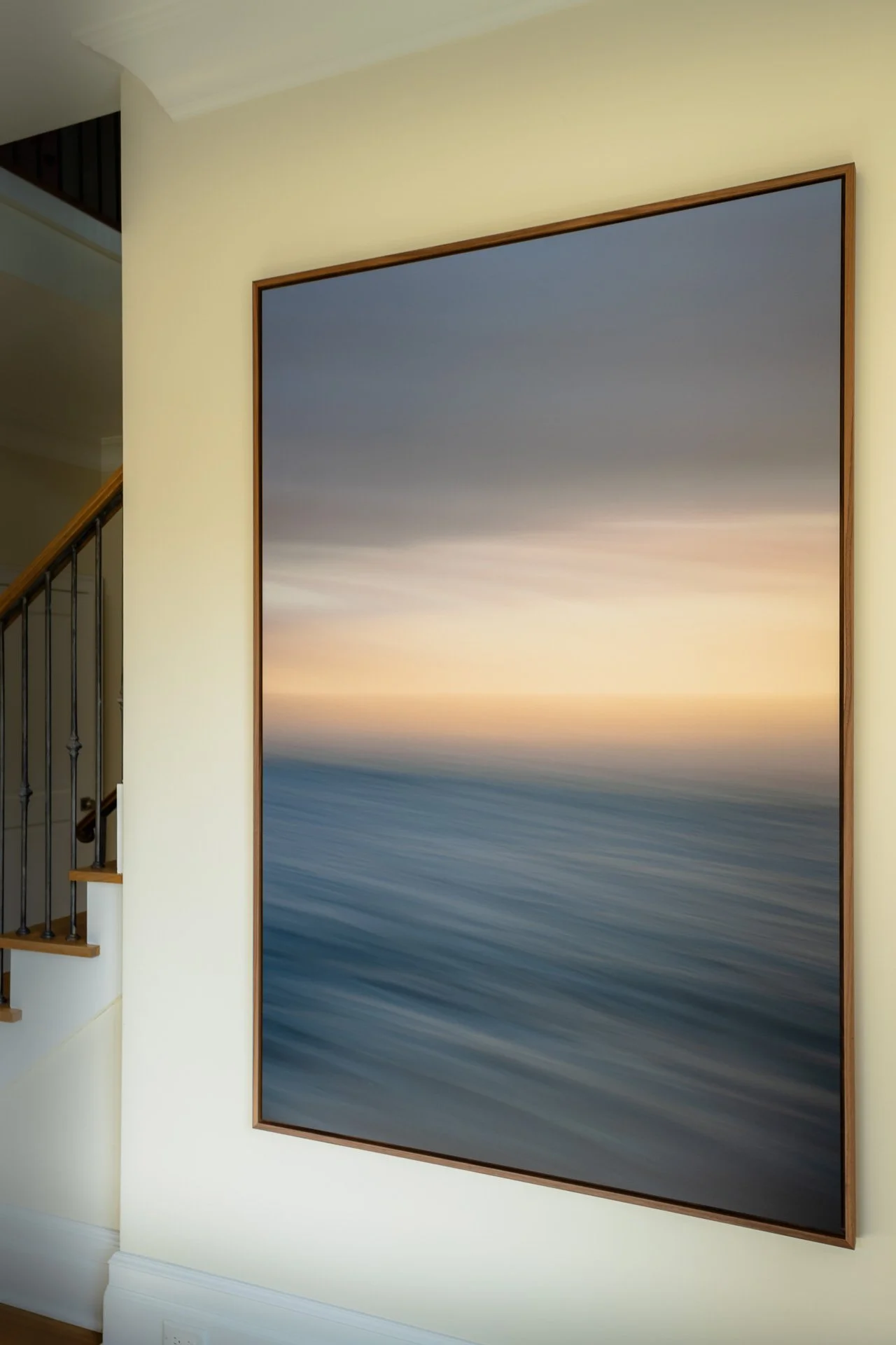 Angled view of Break in the Sky beside the staircase, showing the walnut float frame and the soft dusk light of the print