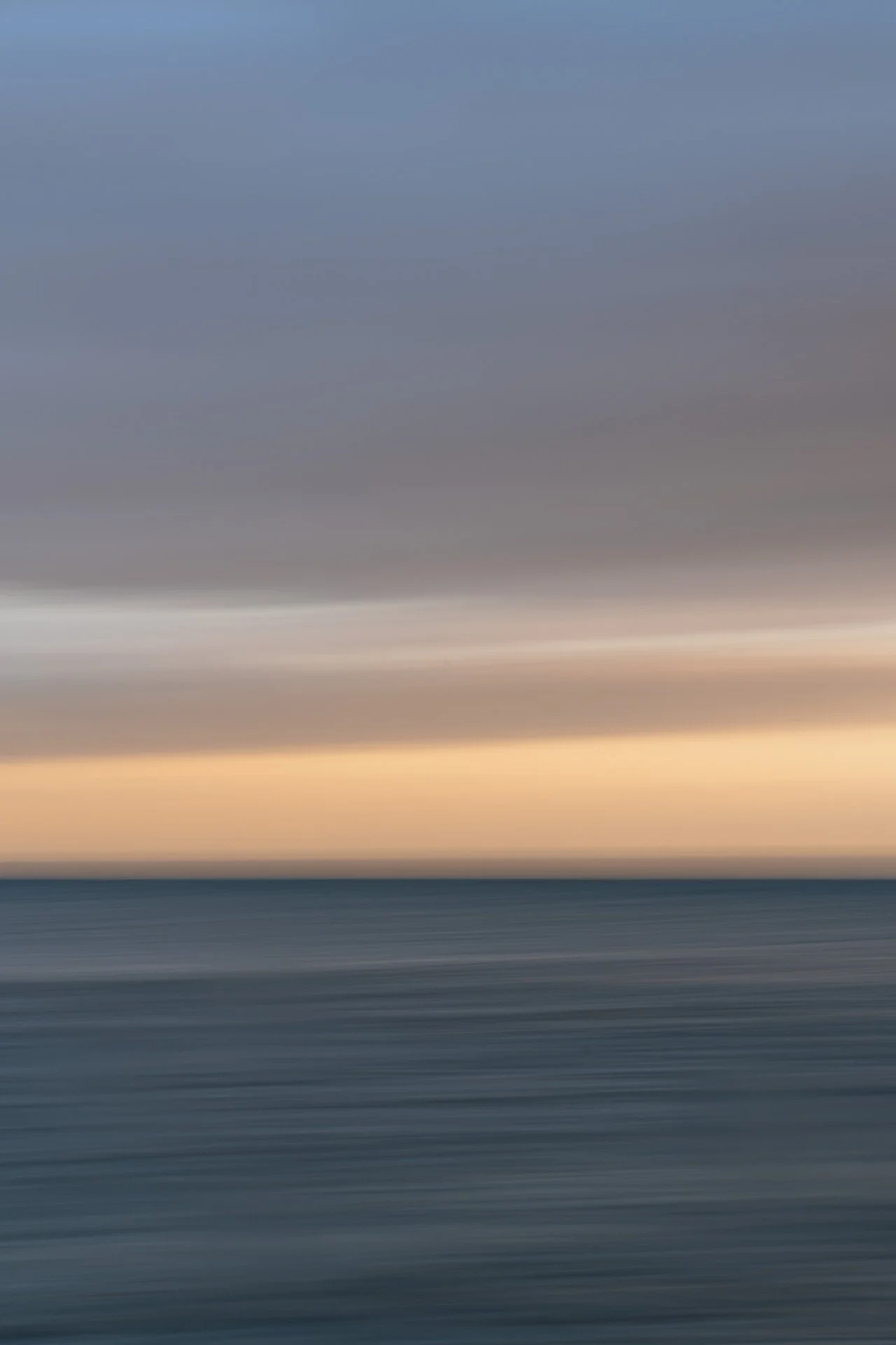 Detail of Break in the Sky: slow-shutter ocean at Rockaway Beach on a May evening, a band of peach light over blue water