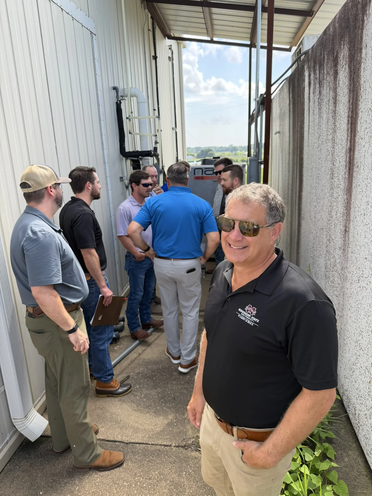 Plant and technical team members discussing equipment and process support outside a poultry processing facility.