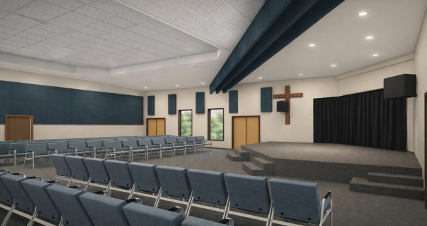 Empty church sanctuary with rows of blue chairs, a small stage, and a wooden cross on the wall.