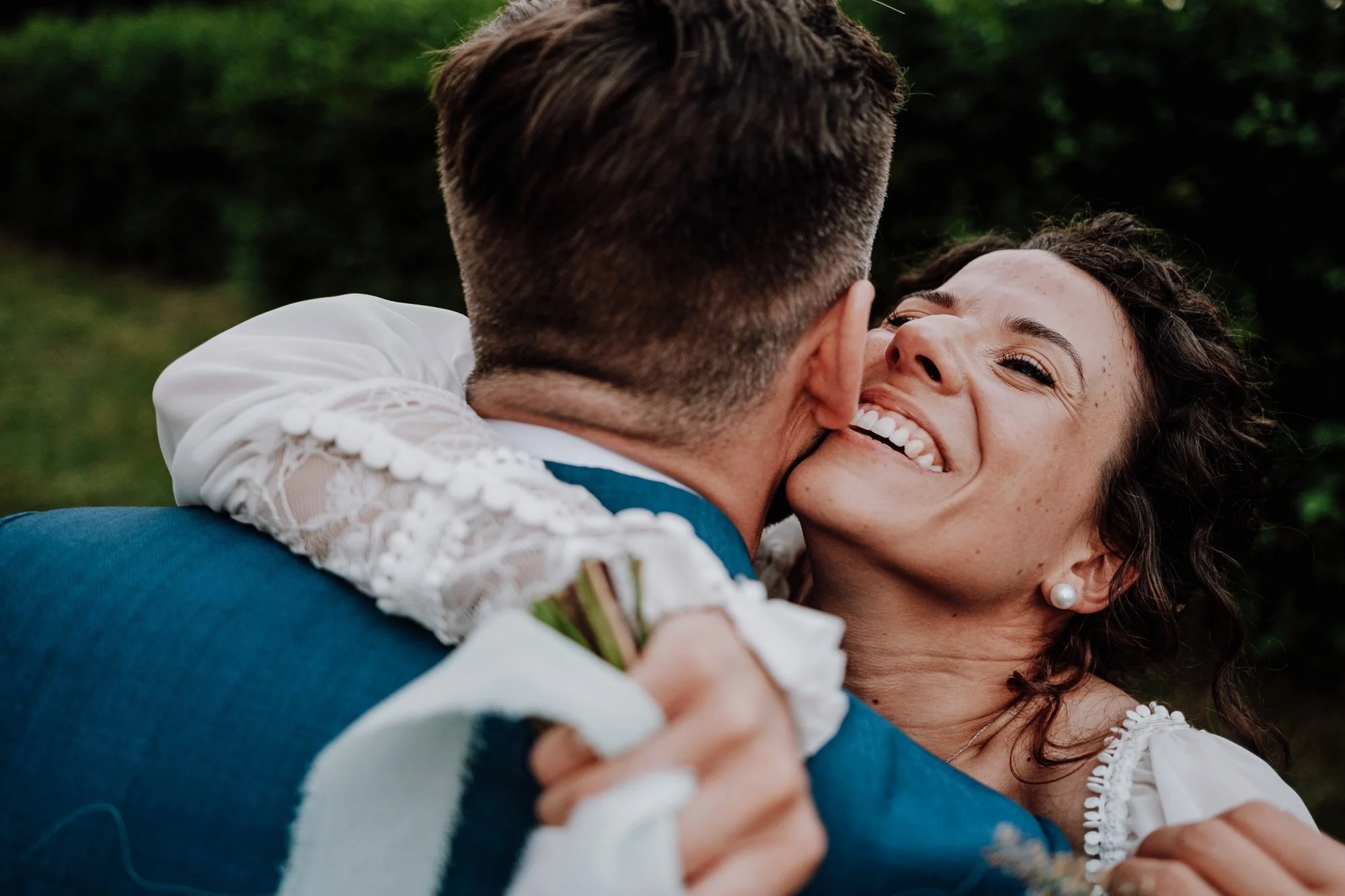 Due persone, un uomo e una donna, si abbracciano felici durante un matrimonio all'aperto, sorridendo con gioia.