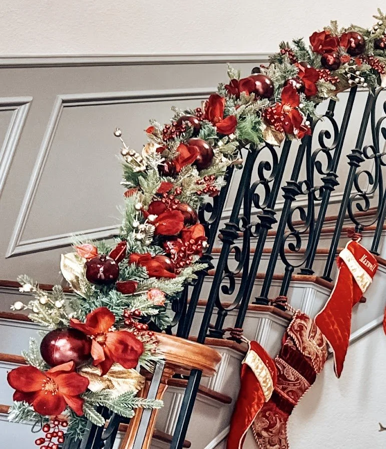 Christmas holiday decor on staircase railing, including red ornaments, poinsettias, and stockings.